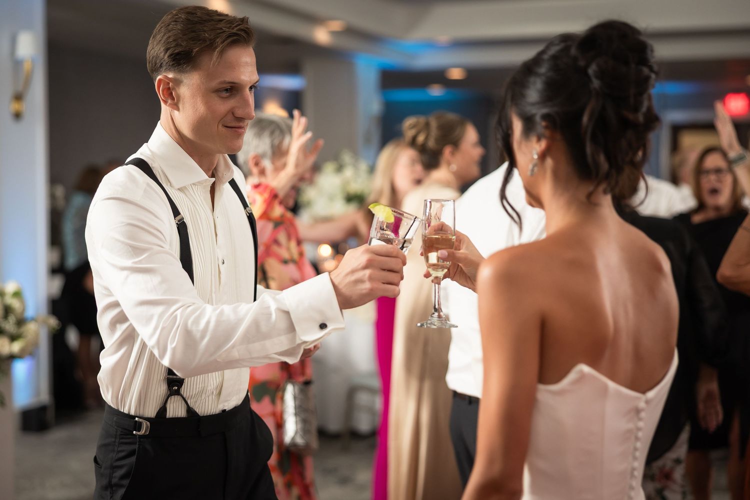 Wedding party members in formal attire dance and celebrate at an indoor reception.