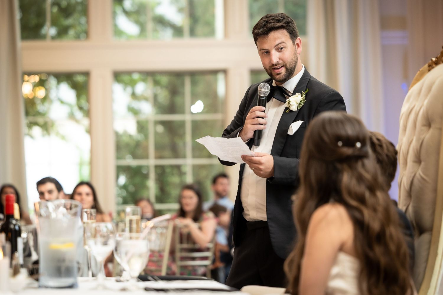 Wedding reception in an elegant white room with large windows and crystal chandeliers.
