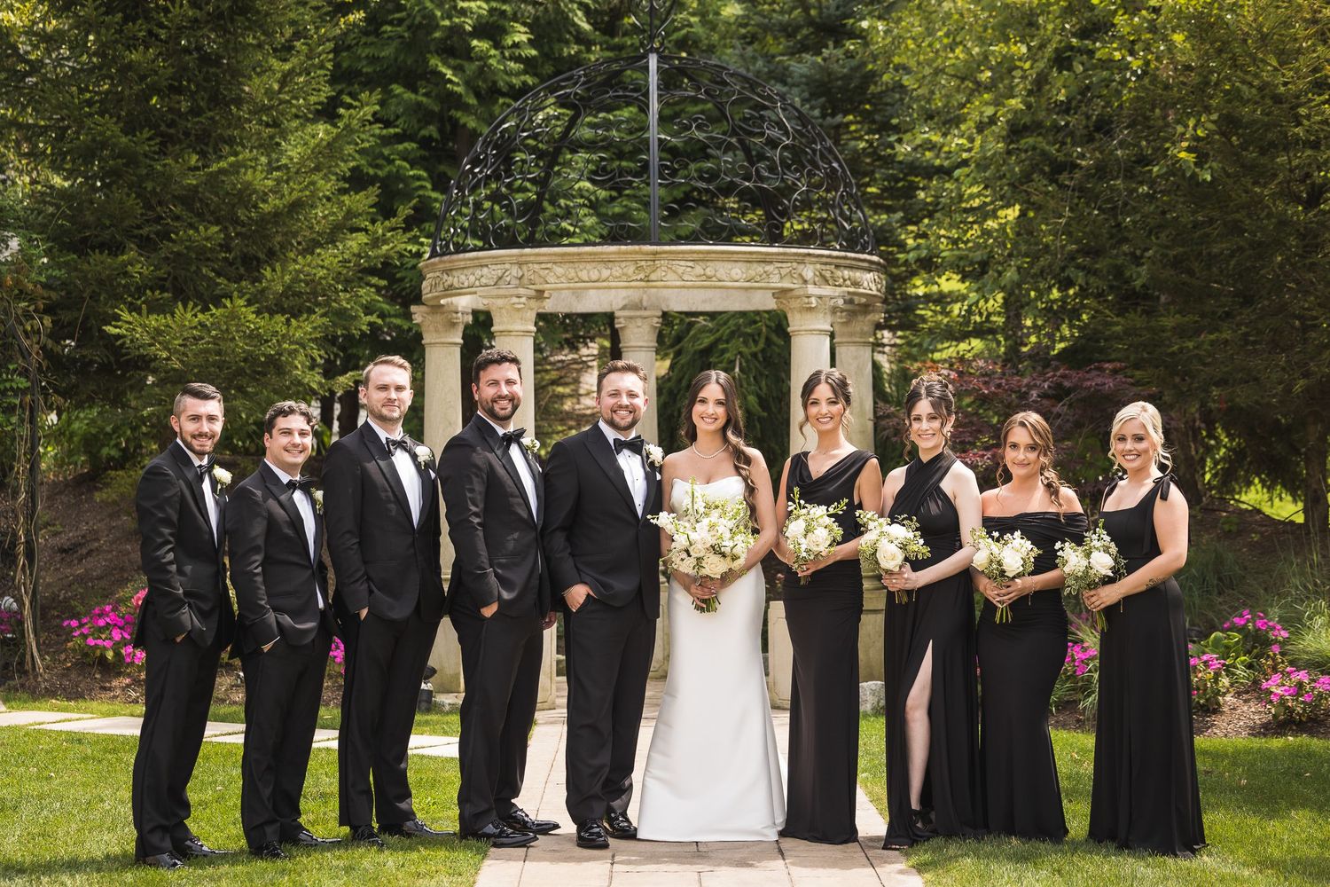 Wedding party in black and white attire posing outdoors in a garden setting.