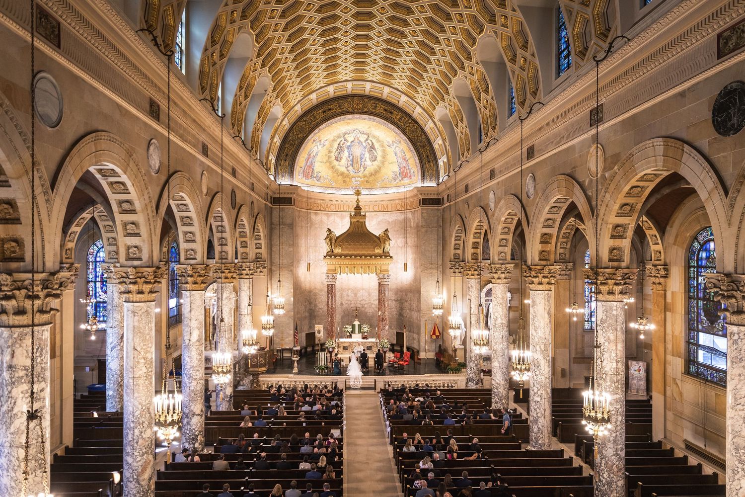 Panoramic view of ornate church interior with vaulted ceilings and stained glass windows.