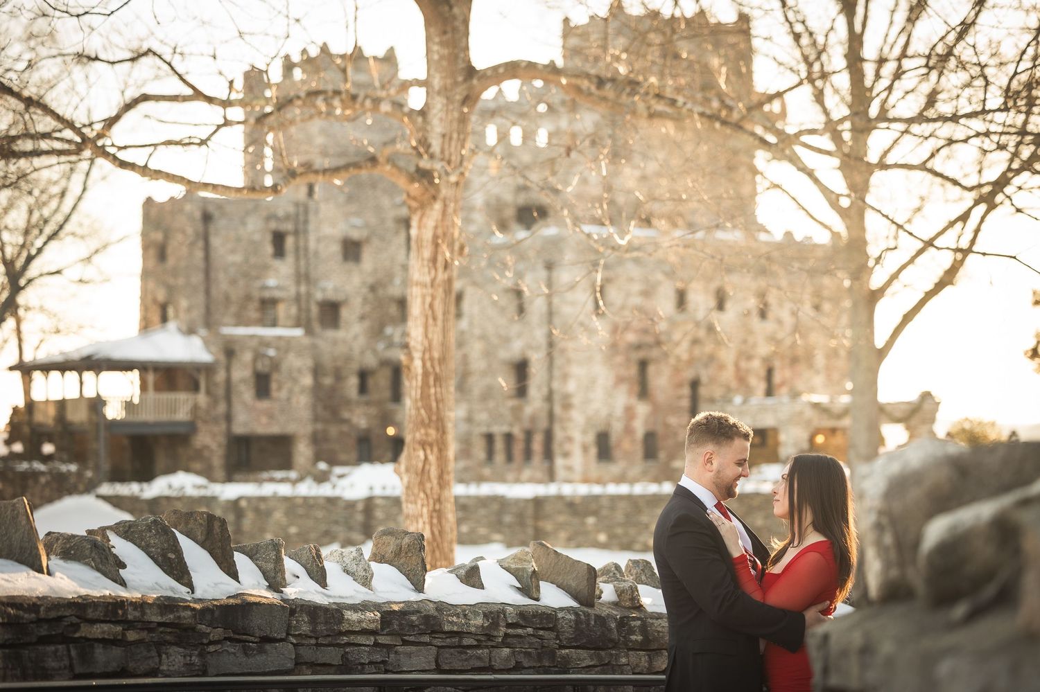 A couple shares a romantic moment in front of a historic stone castle during sunset.