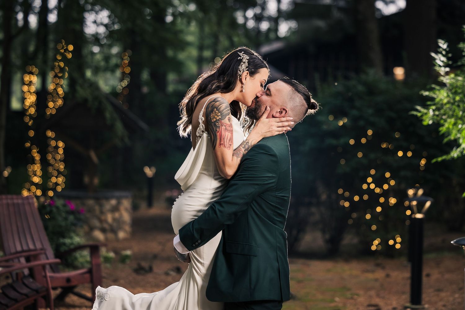 A romantic couple shares a kiss in a forest setting with twinkling lights and trees in the background.