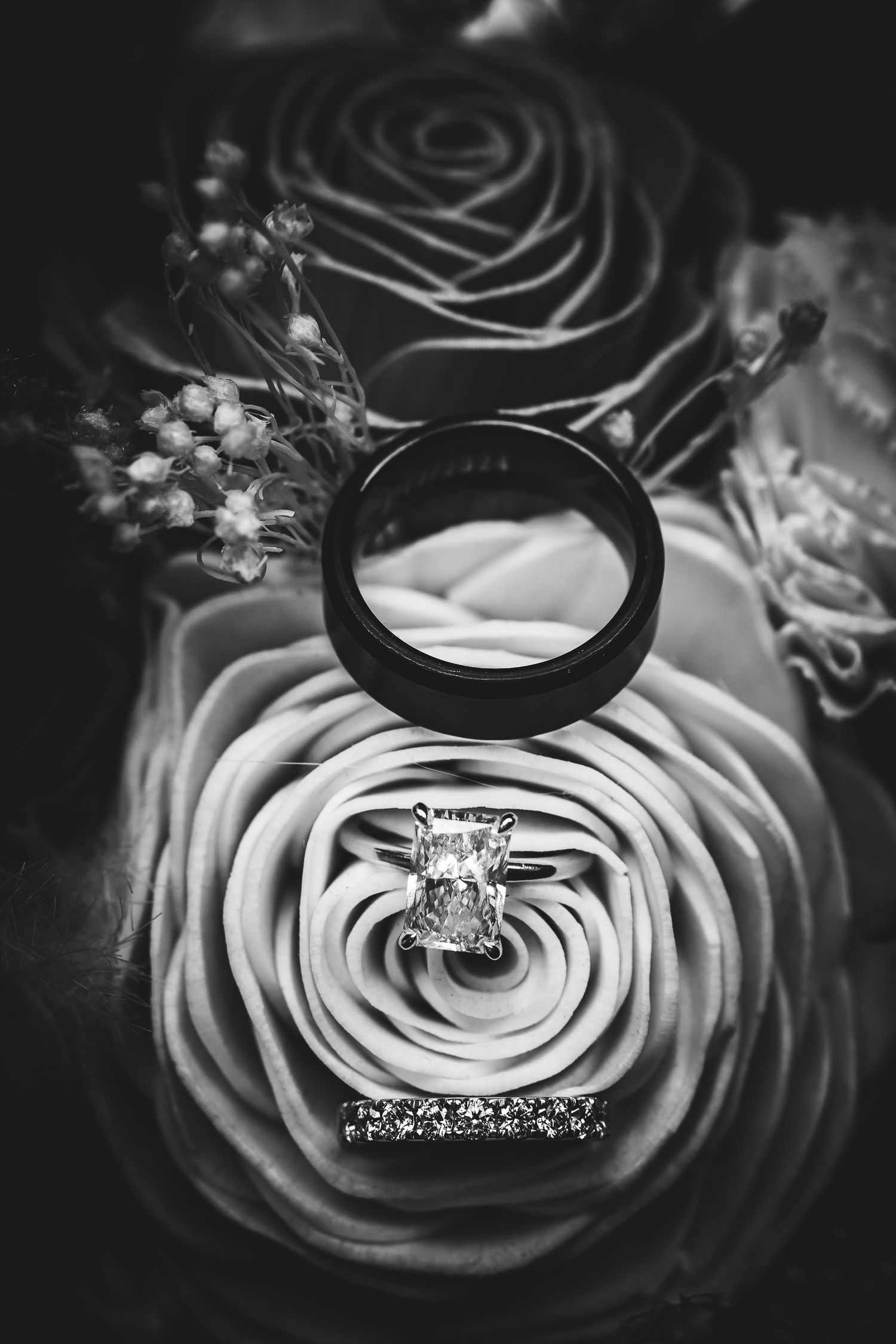 Black and white macro photography of wedding rings nestled in delicate rose petals creating an elegant artistic composition.