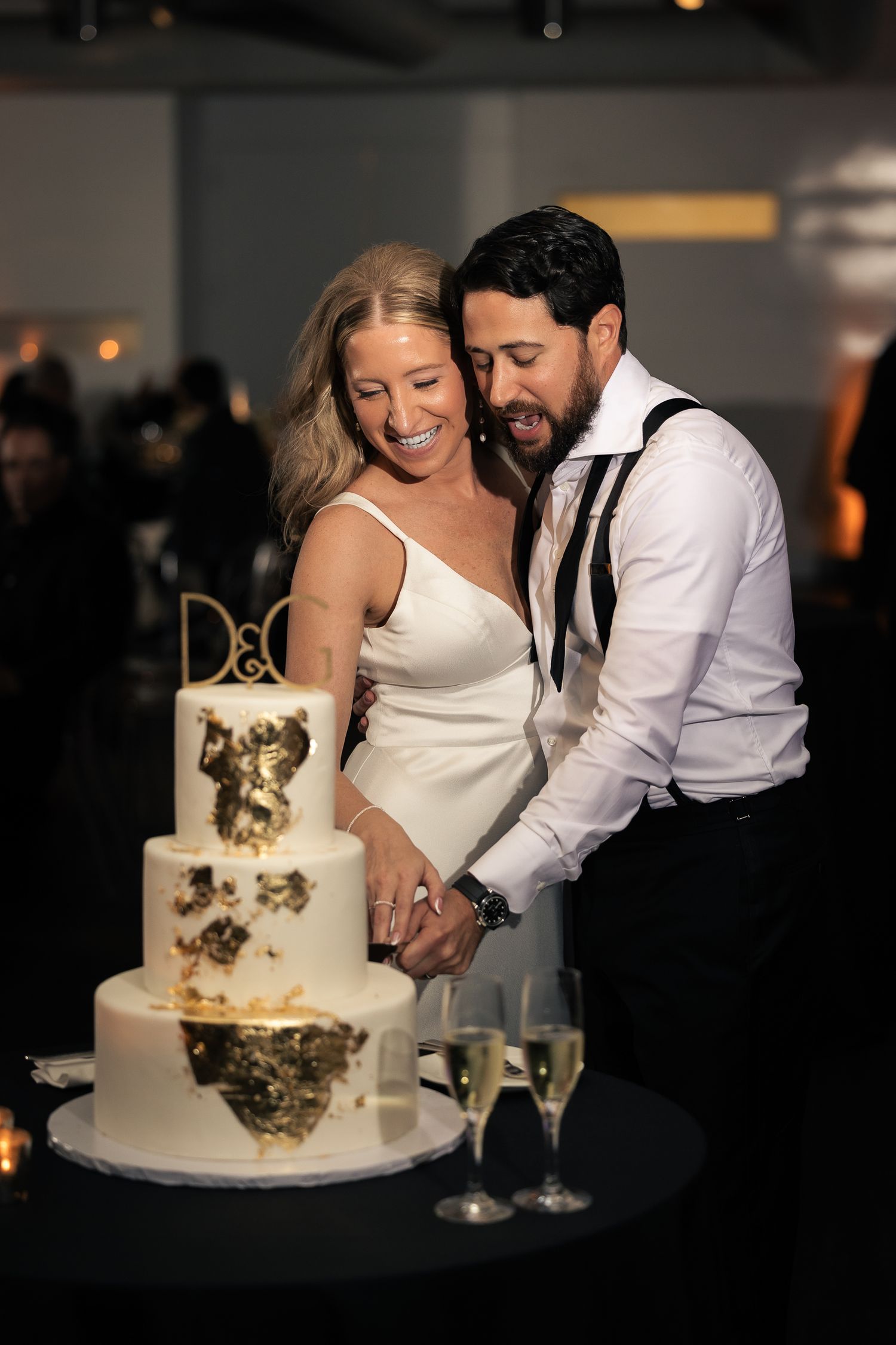 A bride and groom cut their elegant white and gold wedding cake together in a romantic reception setting.