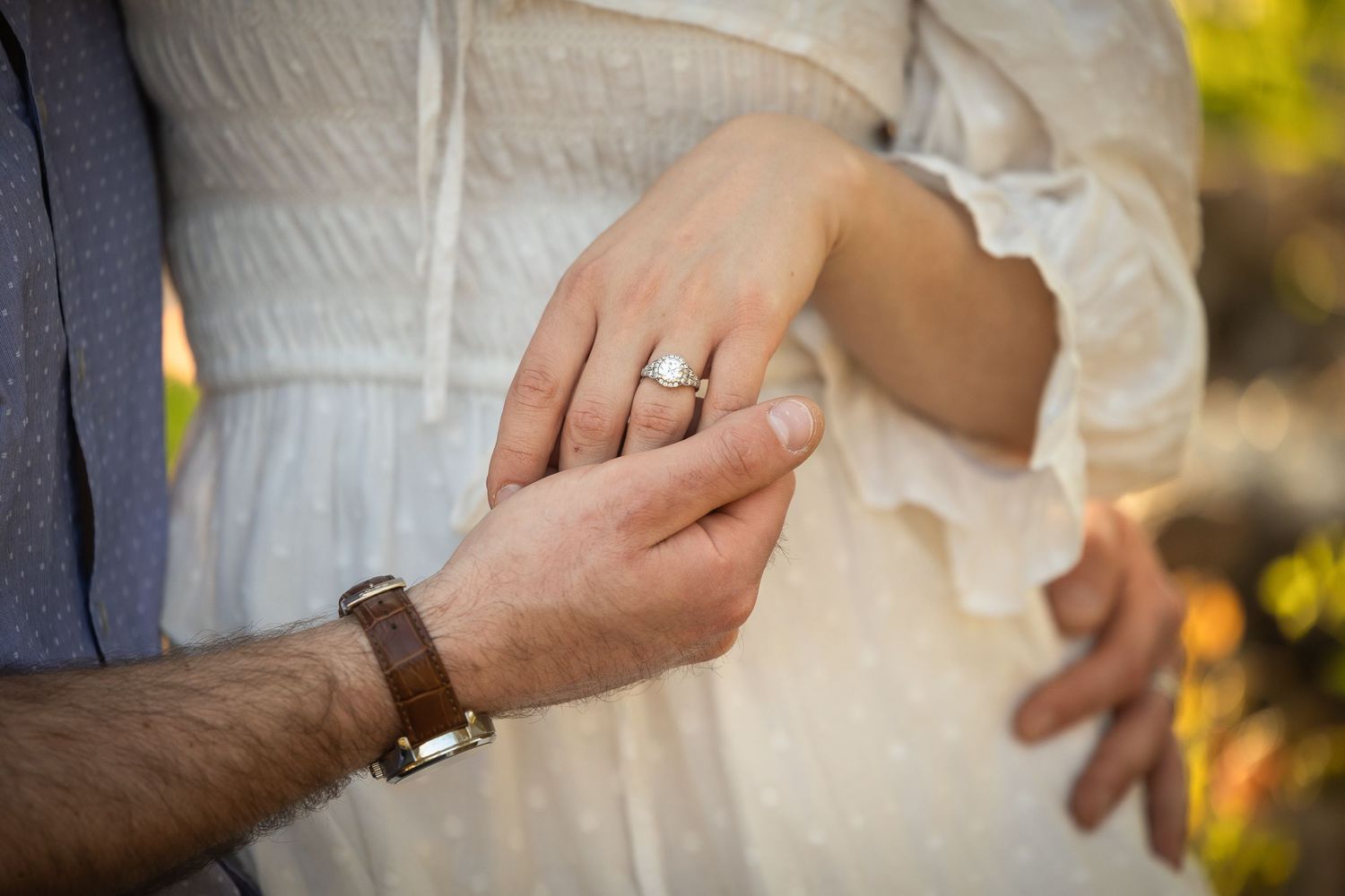 Close-up view of hands exchanging wedding rings during an outdoor ceremony with golden sunlight in background.