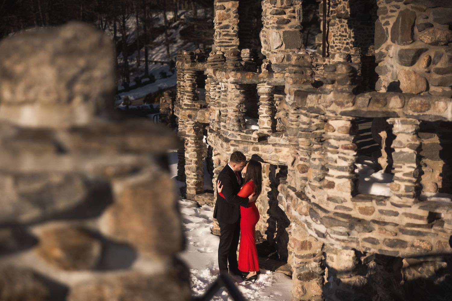 Two people walk through a stone archway corridor with dramatic lighting and architectural details.