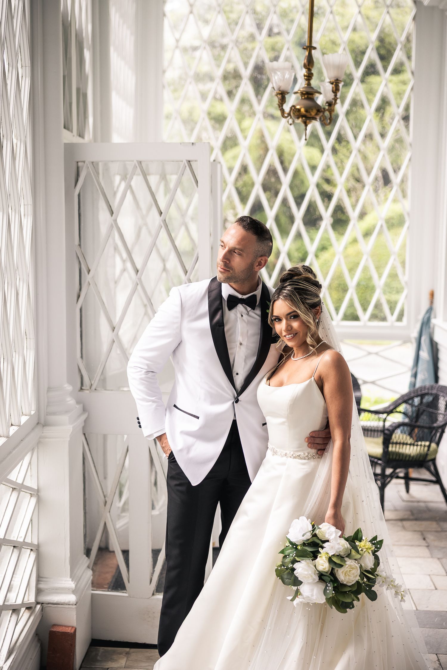 Romantic wedding couple posing in an elegant white latticed porch setting.