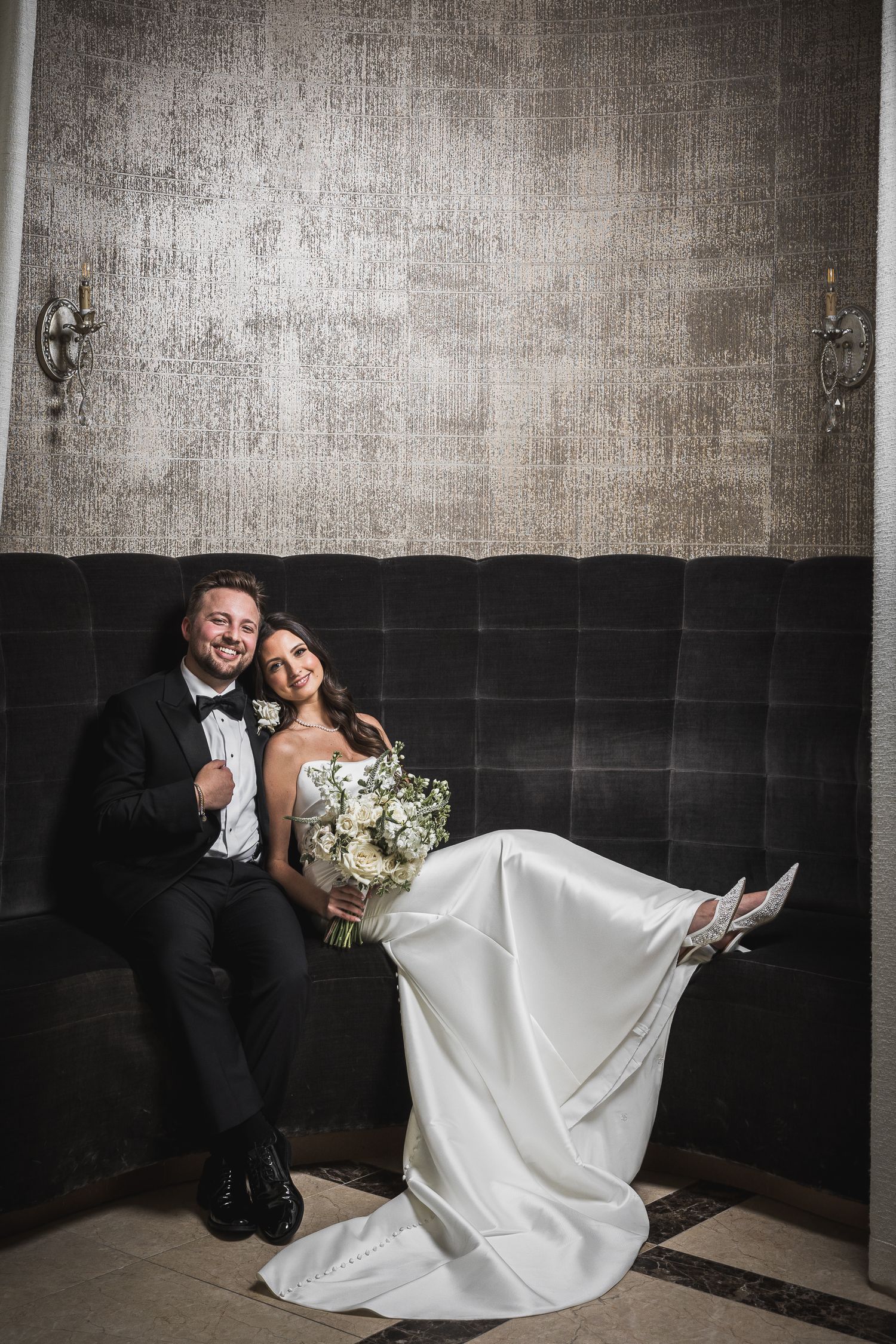 Artistic wedding portrait against textured wall with dramatic lighting and flowing dress.