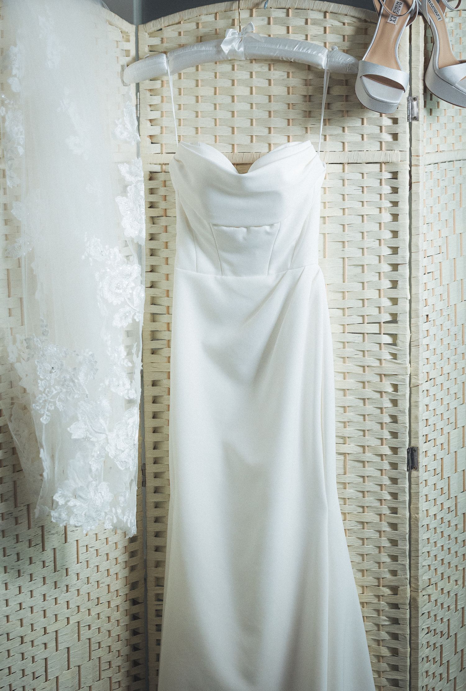 Wedding dress displayed on hanger against textured white wall.