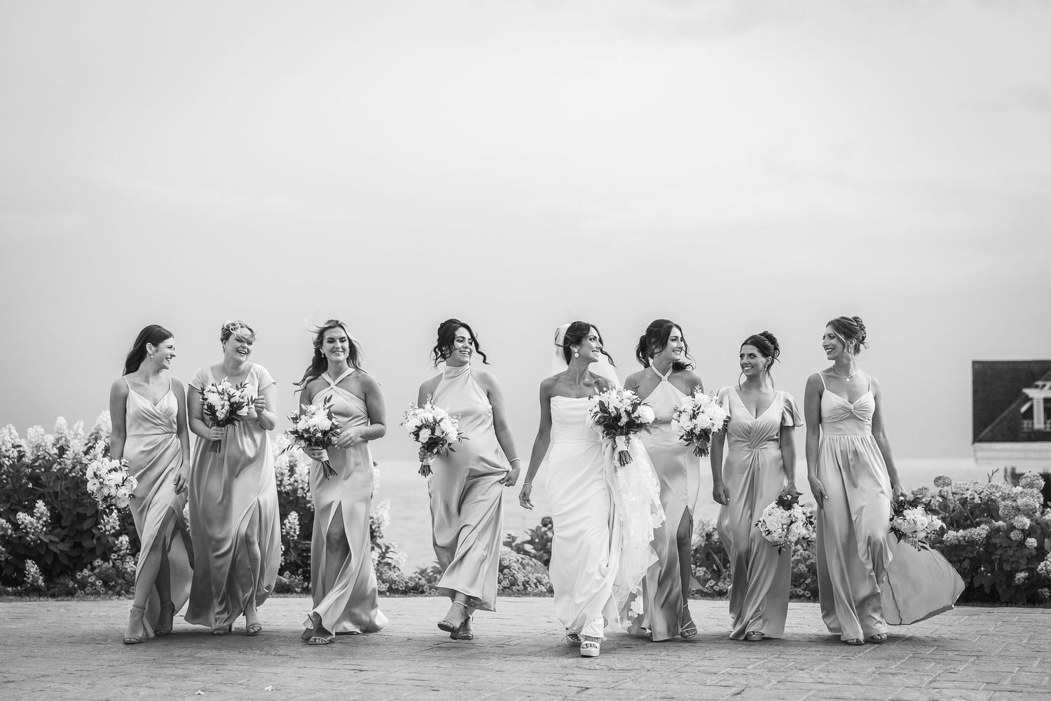 Wedding party in neutral dresses dancing and celebrating on outdoor terrace.