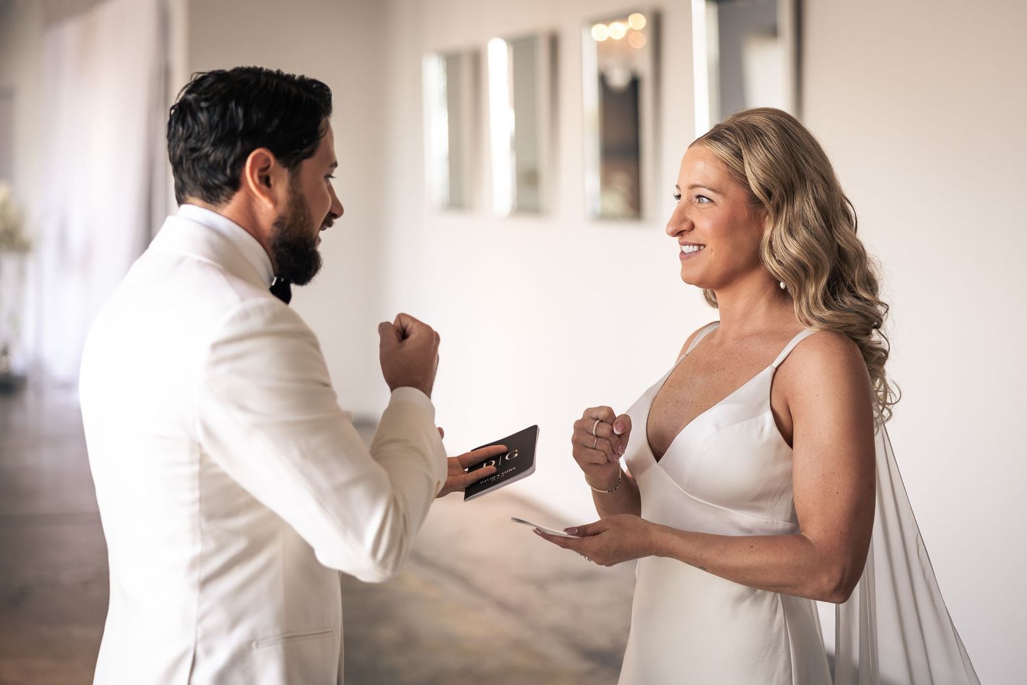 A happy couple shares a playful first look moment in a bright indoor setting with natural lighting.