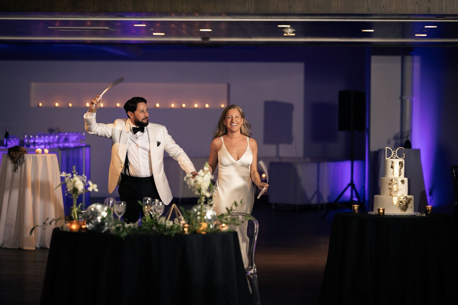Wedding reception venue decorated with blue uplighting and elegant white floral centerpieces on dining tables.