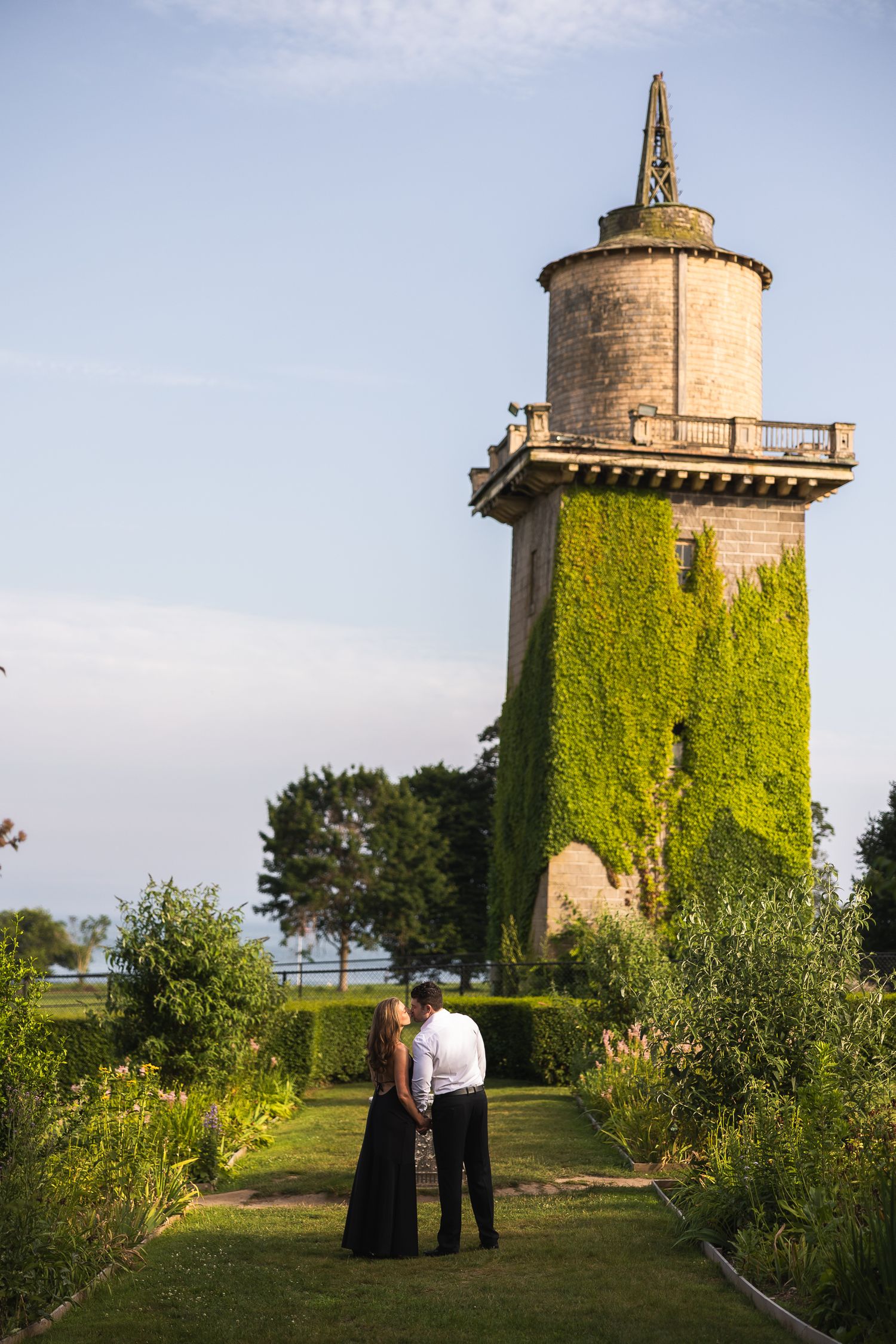 Historic stone tower covered in green ivy stands against blue sky near waterfront.