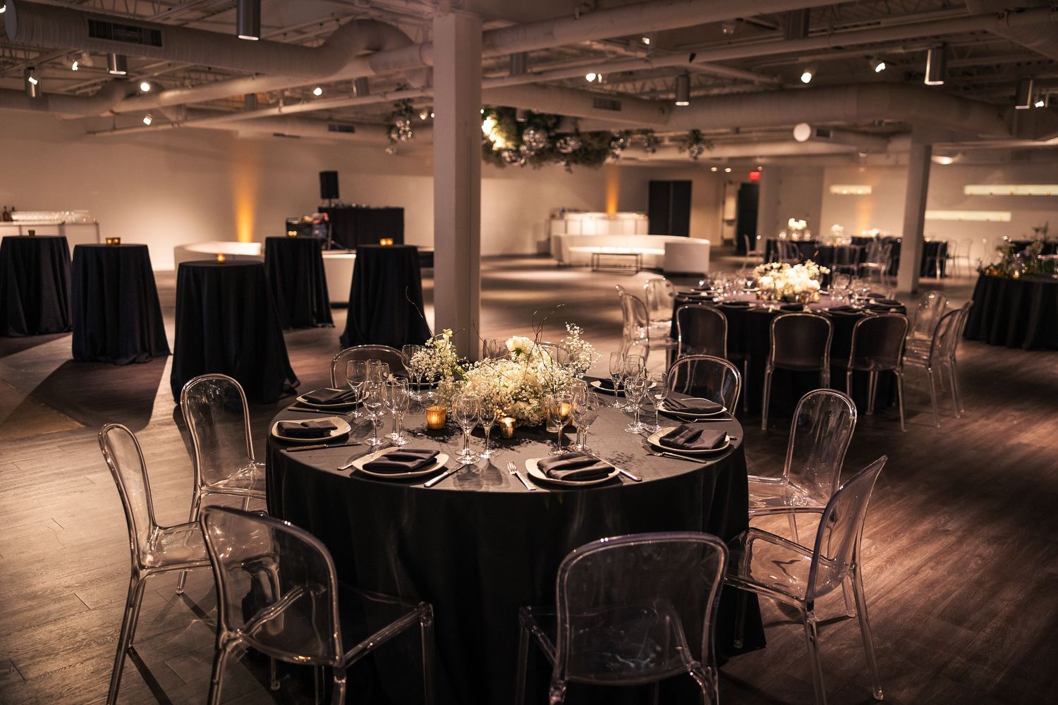 Modern industrial wedding reception venue with round tables and elegant place settings under ambient lighting.