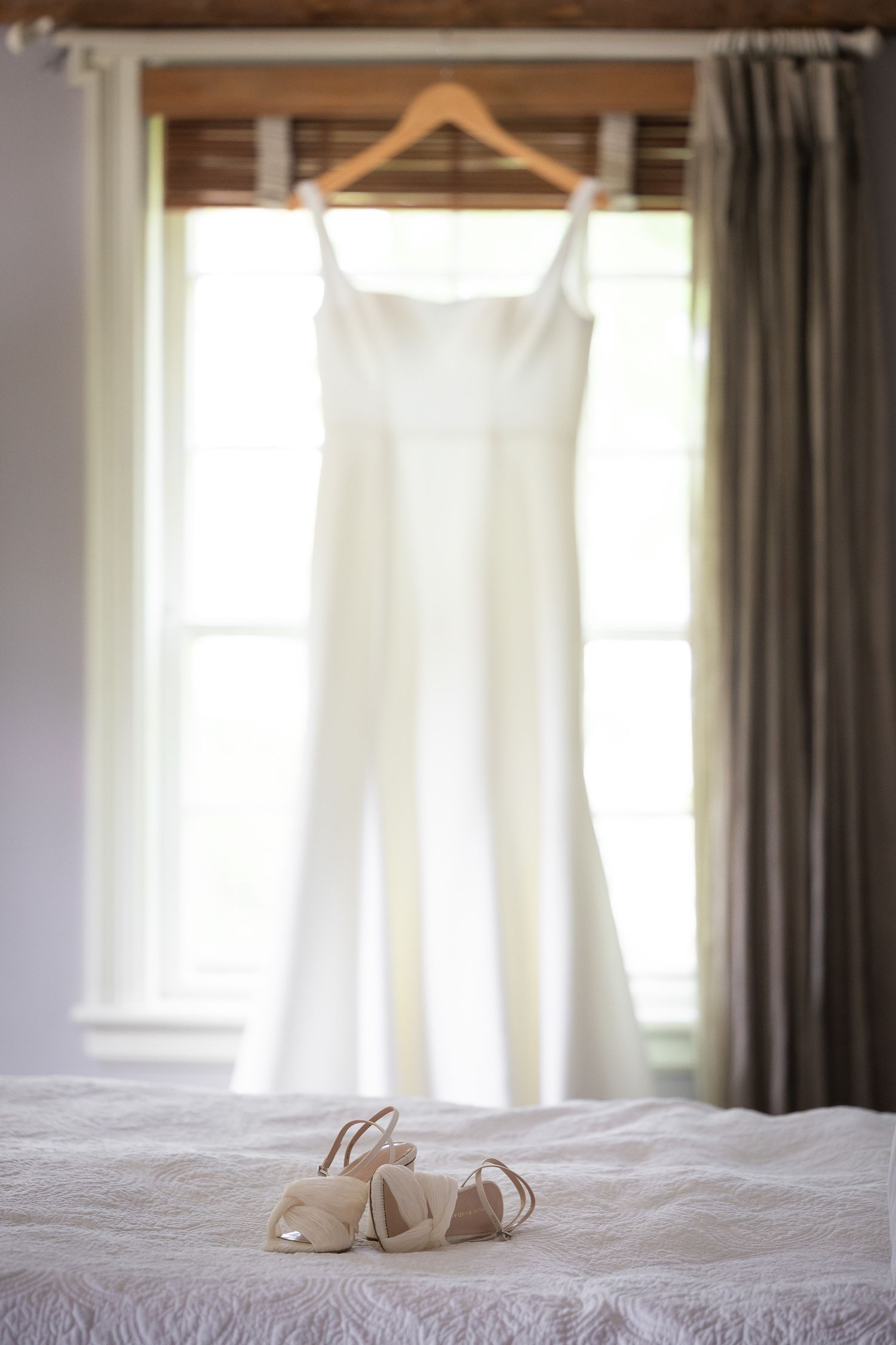 Bridal shoes and white dress displayed in a bright room with window light.