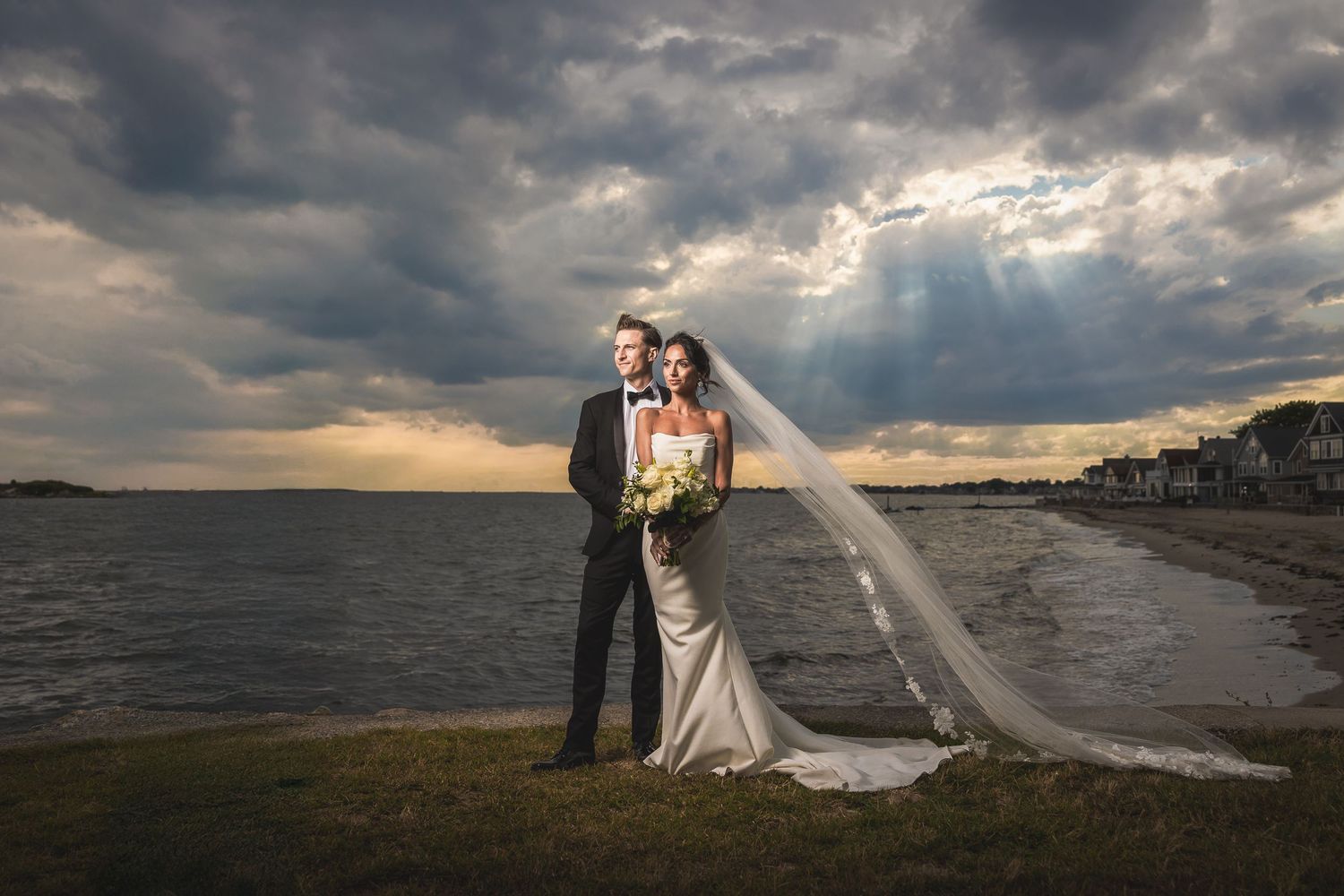 Dramatic sunset wedding portrait on beach with stormy clouds and flowing veil.