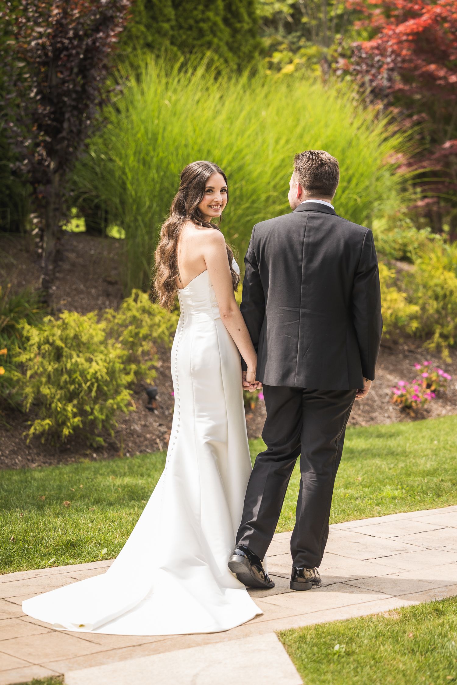 Wedding couple walking along garden path surrounded by lush greenery and colorful foliage.