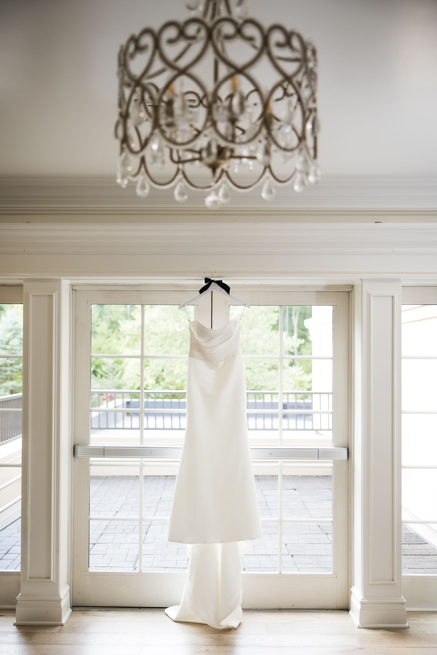 Wedding gowns displayed under ornate chandelier in bright white bridal boutique.