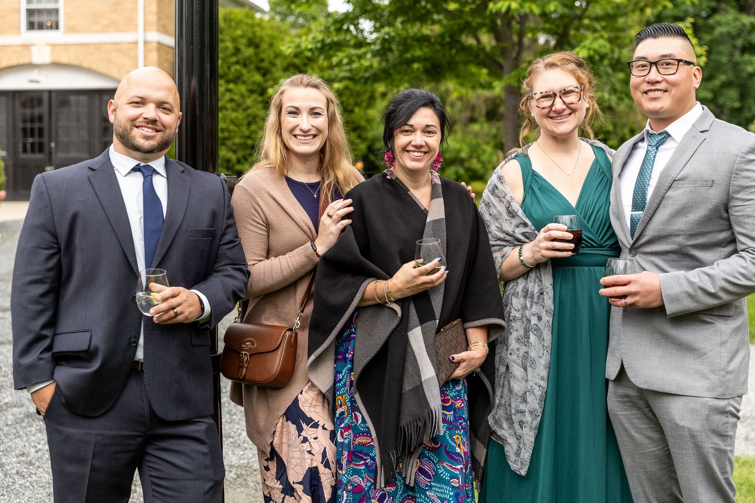 Wedding guests in formal attire gather outdoors for group photos.