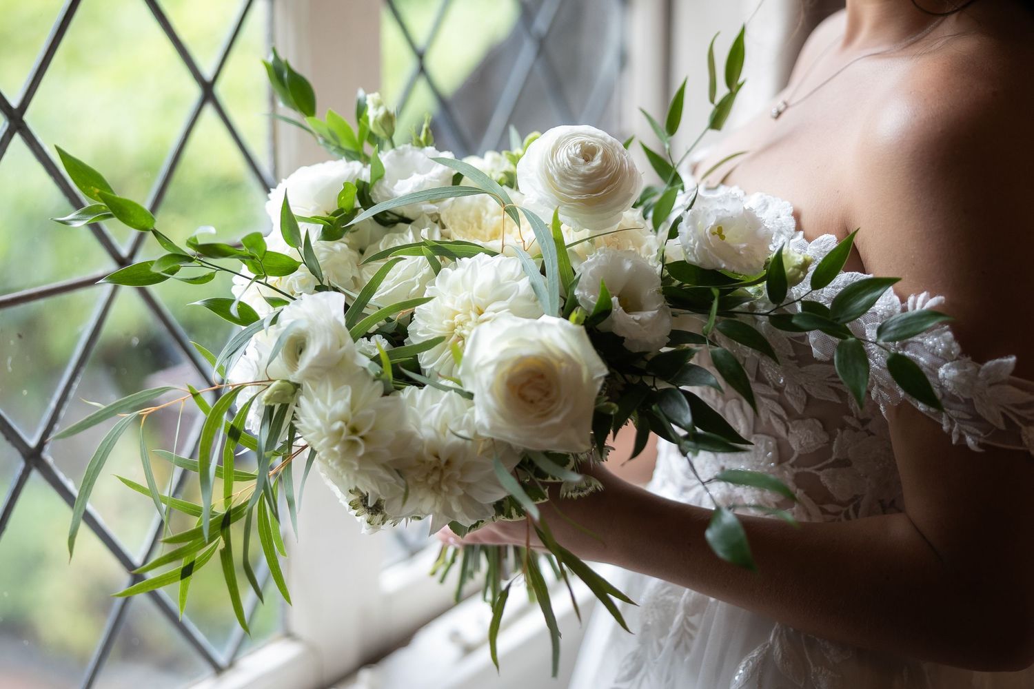 Elegant white wedding bouquet with roses and greenery in soft natural light.