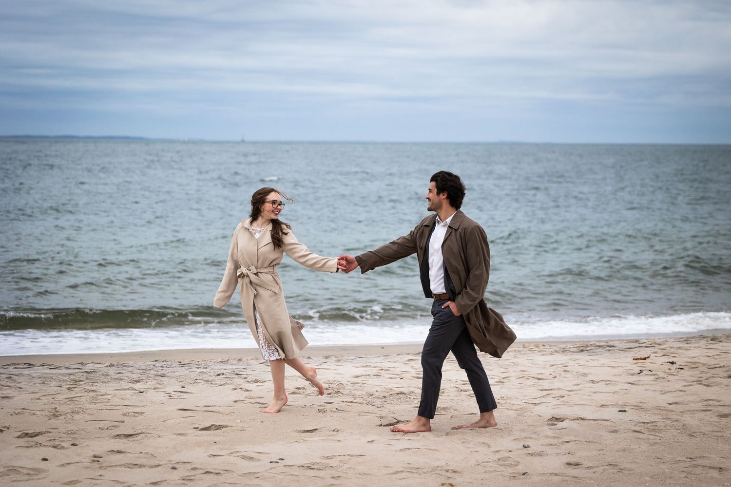 Romantic beach photoshoot with waves and cloudy skies creating a serene backdrop.