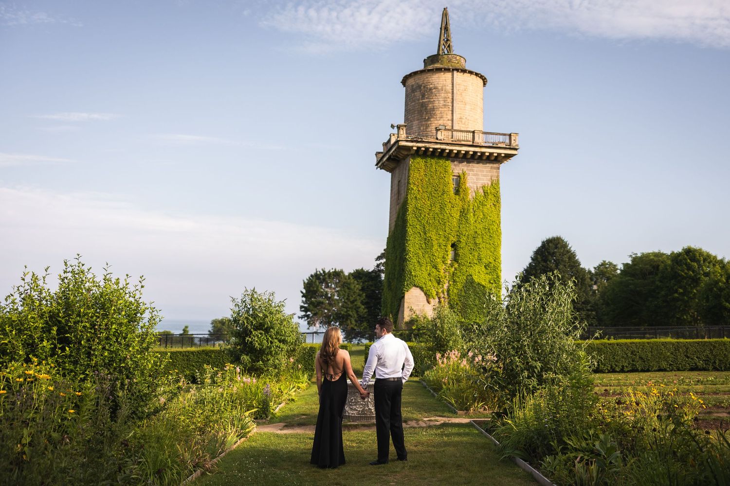 A panoramic view of a rustic windmill in a green countryside field with people standing nearby.