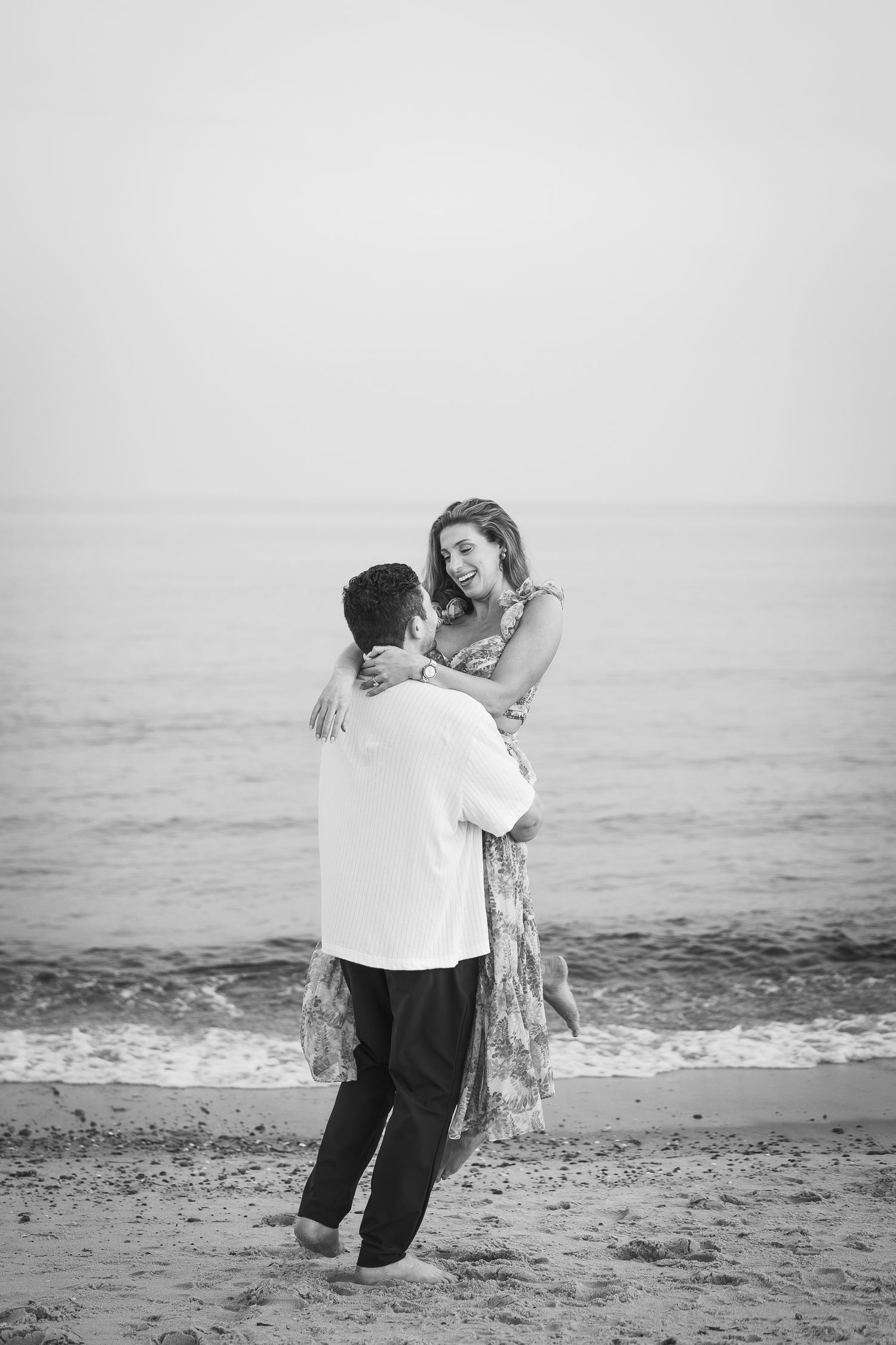 A romantic couple embraces and dances together on a misty beach shore in black and white.