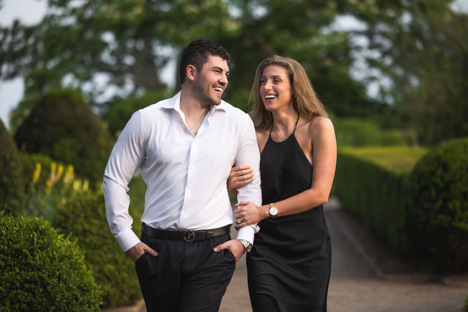 Two people share a joyful conversation while walking through a scenic garden pathway.