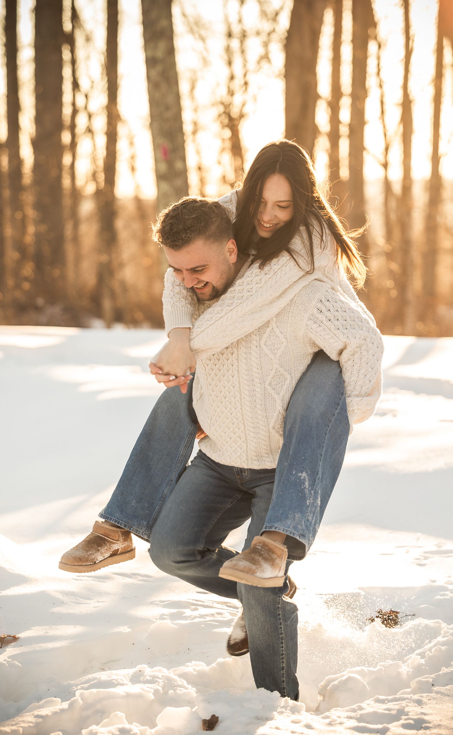 Person sitting in snowy winter landscape wearing cream sweater and jeans during golden sunset in forest.