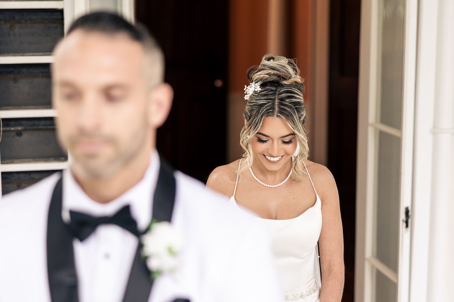 A bride in an elegant white dress smiles while walking through an ornate doorway.