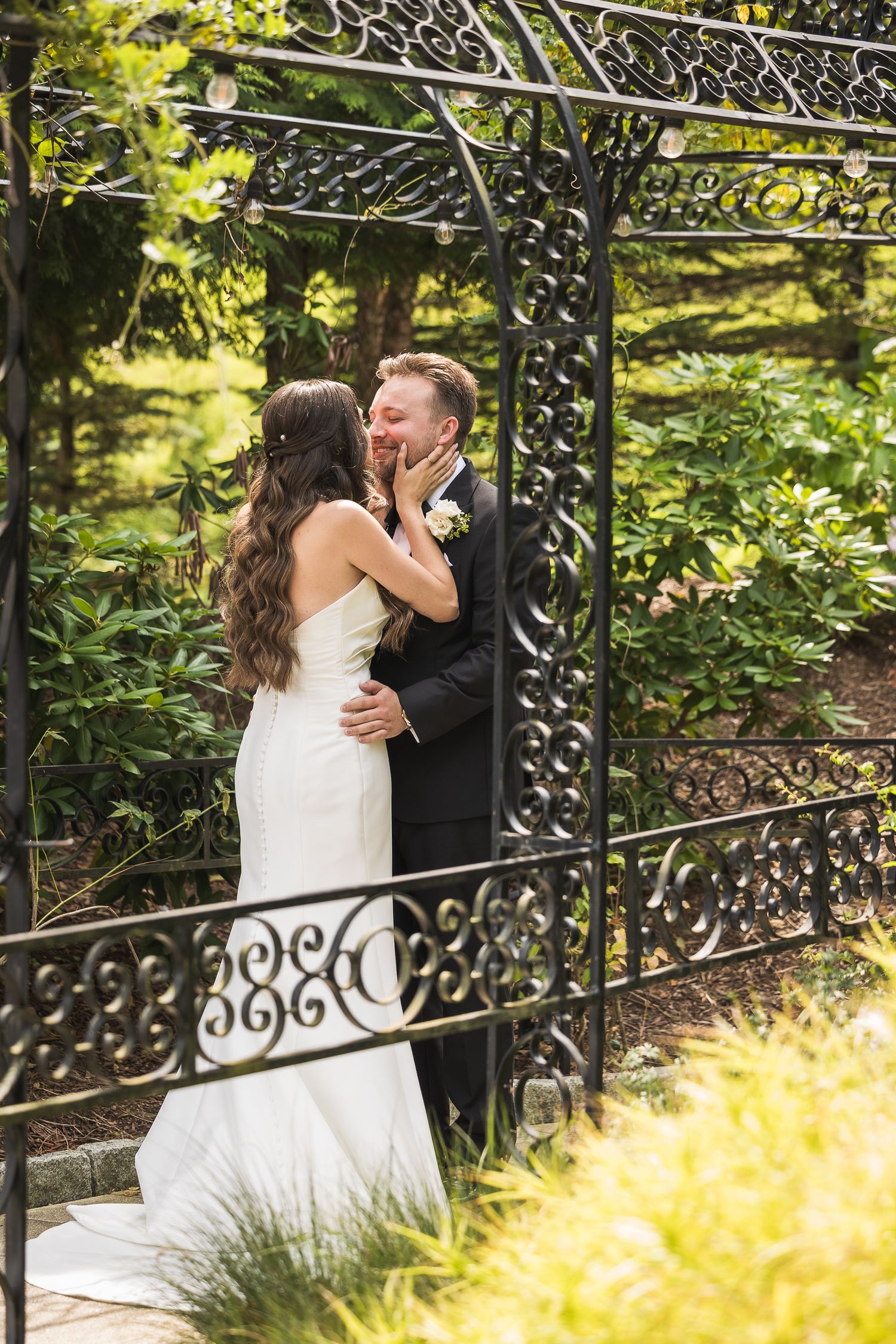 Newlyweds sharing intimate moment by ornate iron garden fence.