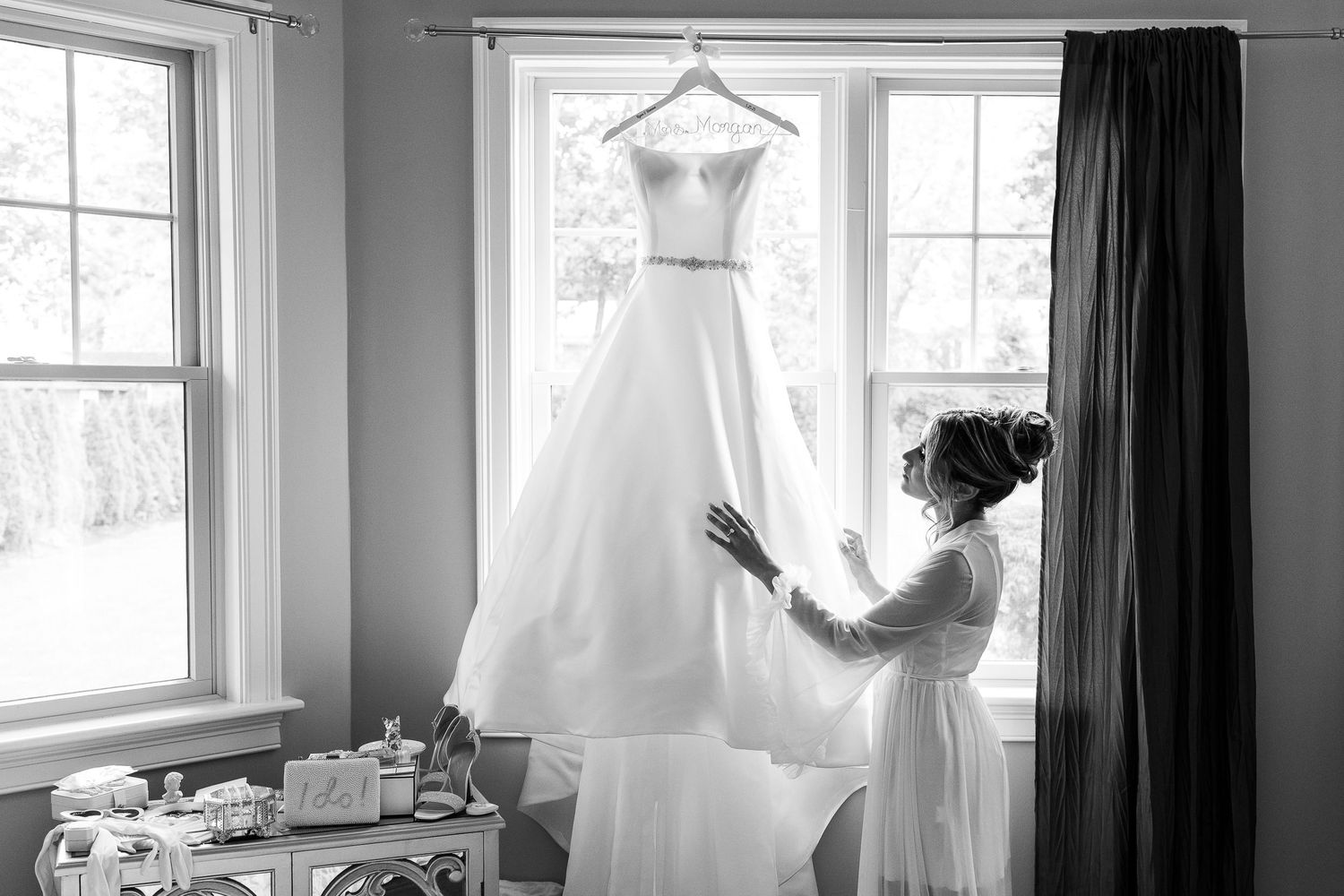 Wedding dress displayed in natural light against windows with dark curtains.