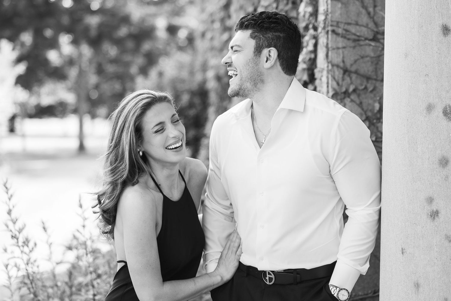 A romantic black and white portrait of a couple laughing together outdoors.