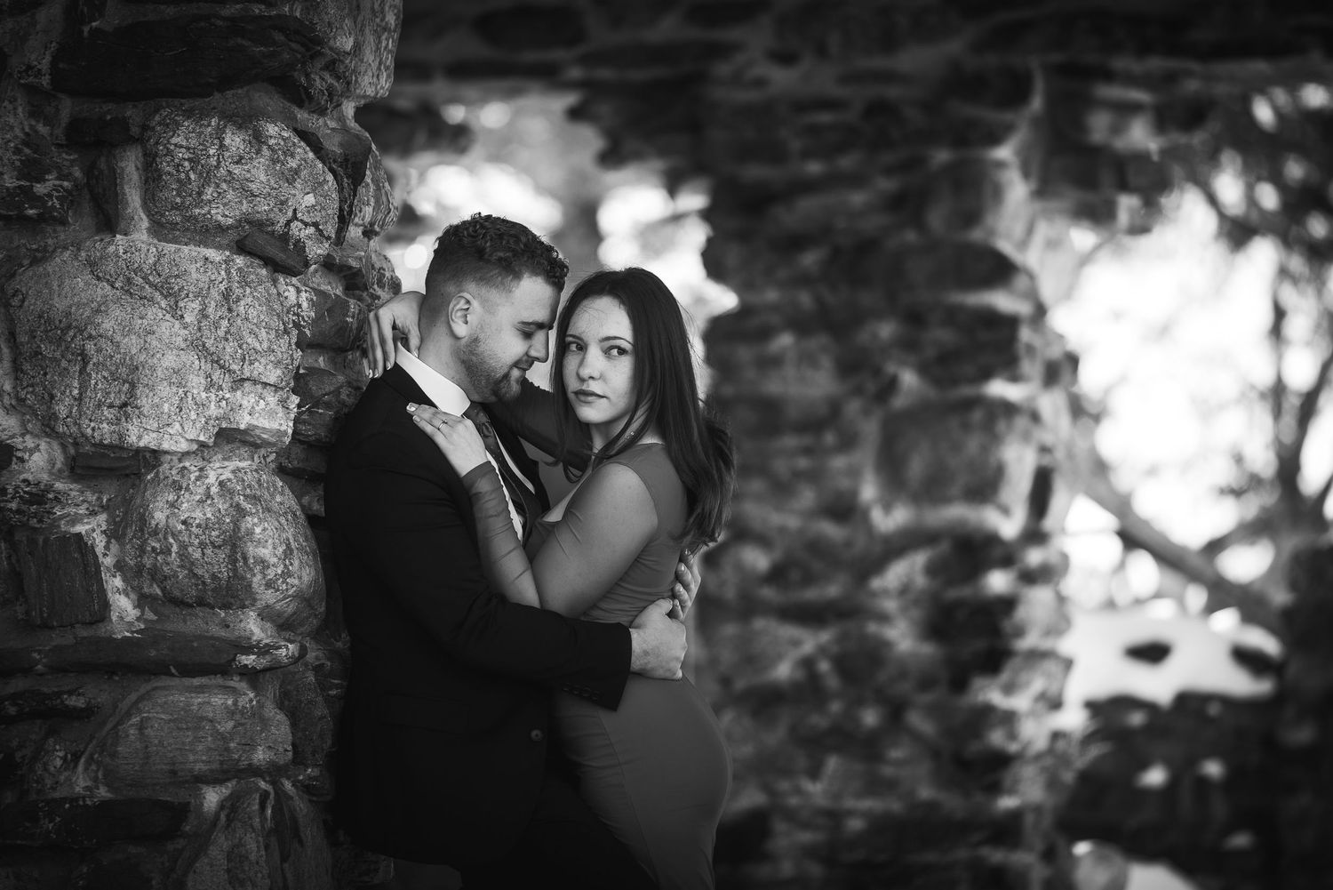 A romantic black and white photo series showing intimate moments between a couple against a stone wall background.