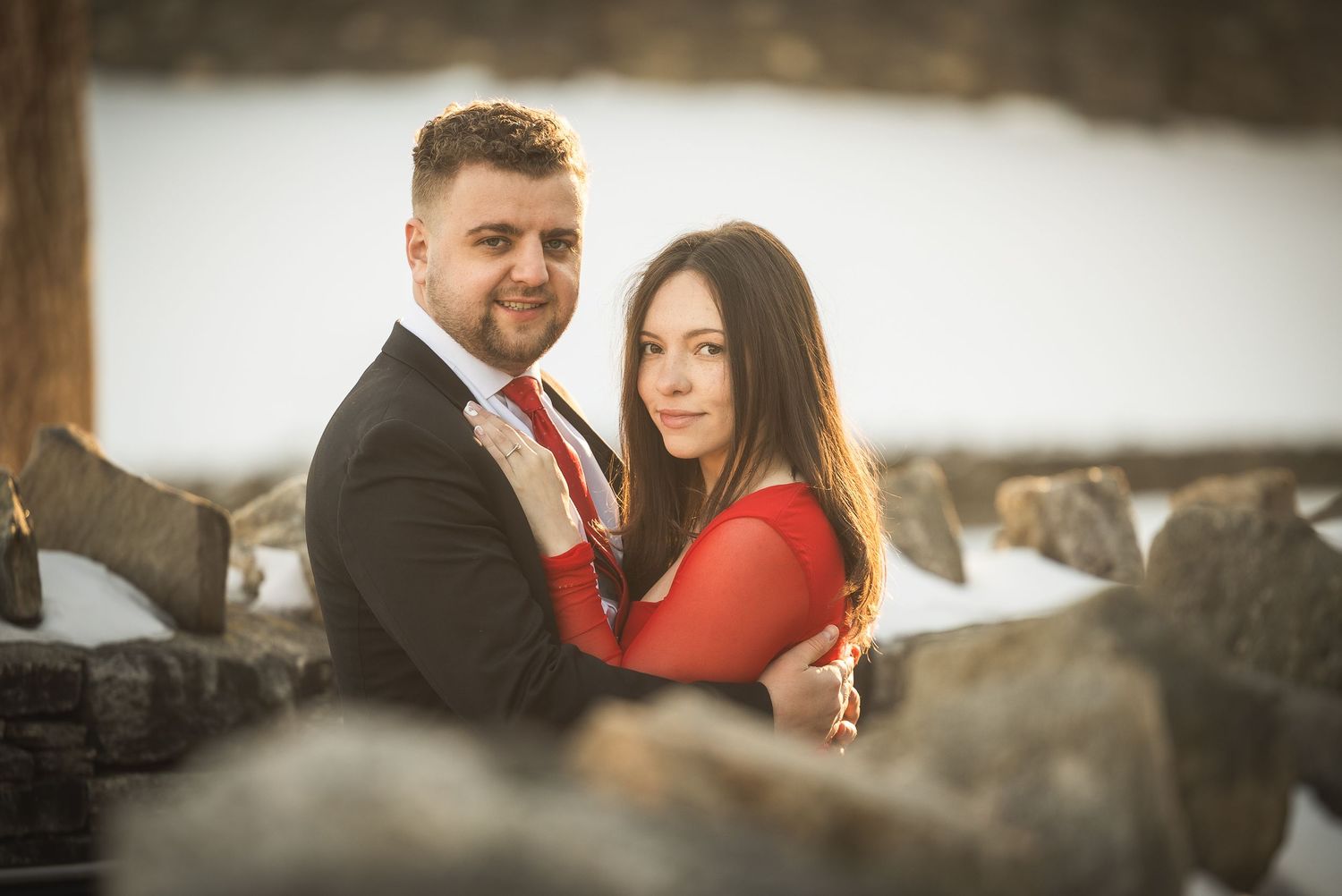 Romantic couple embraces during a winter engagement photoshoot against a snowy mountain backdrop.