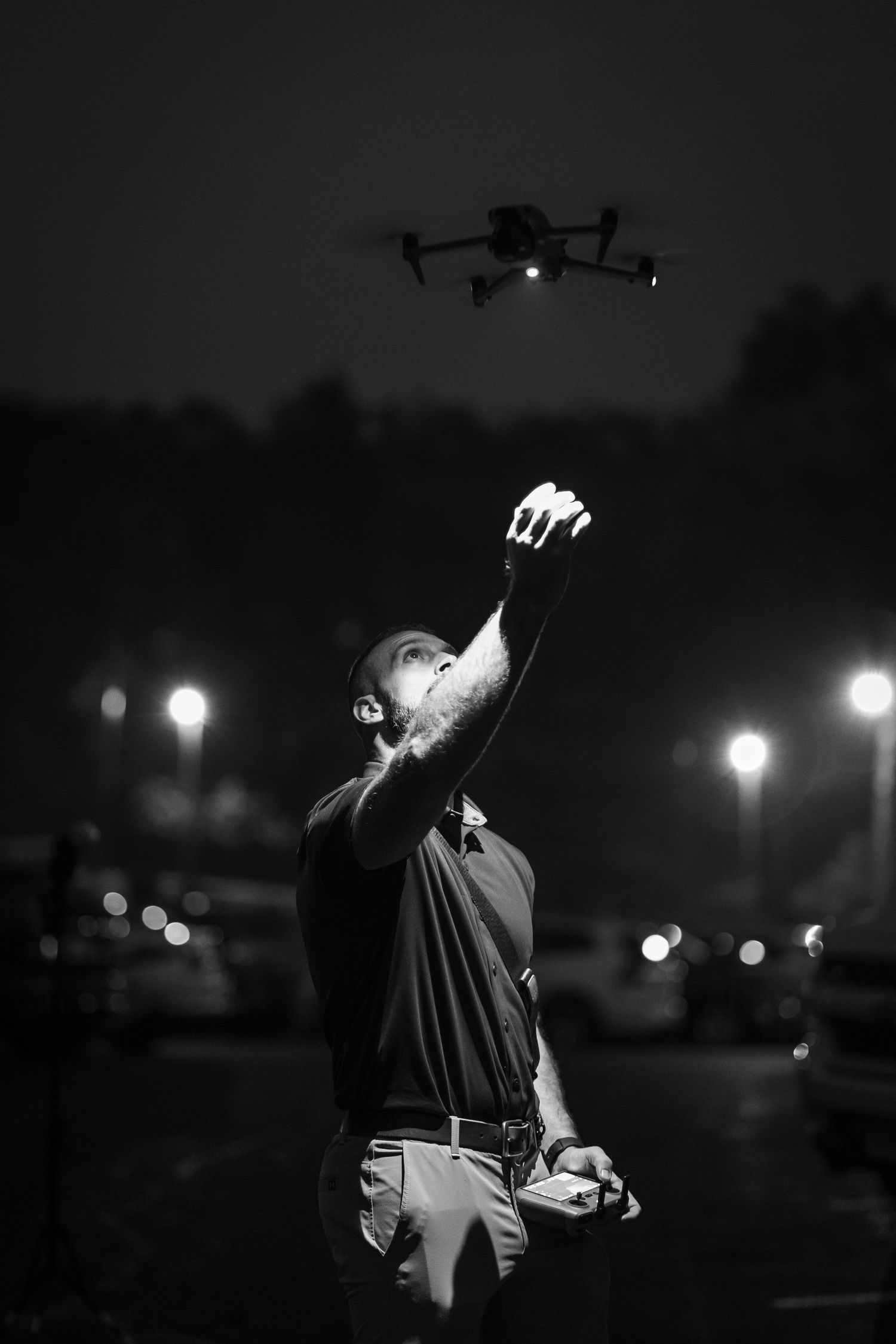 A drone operator works at night with illuminated lights in the background.
