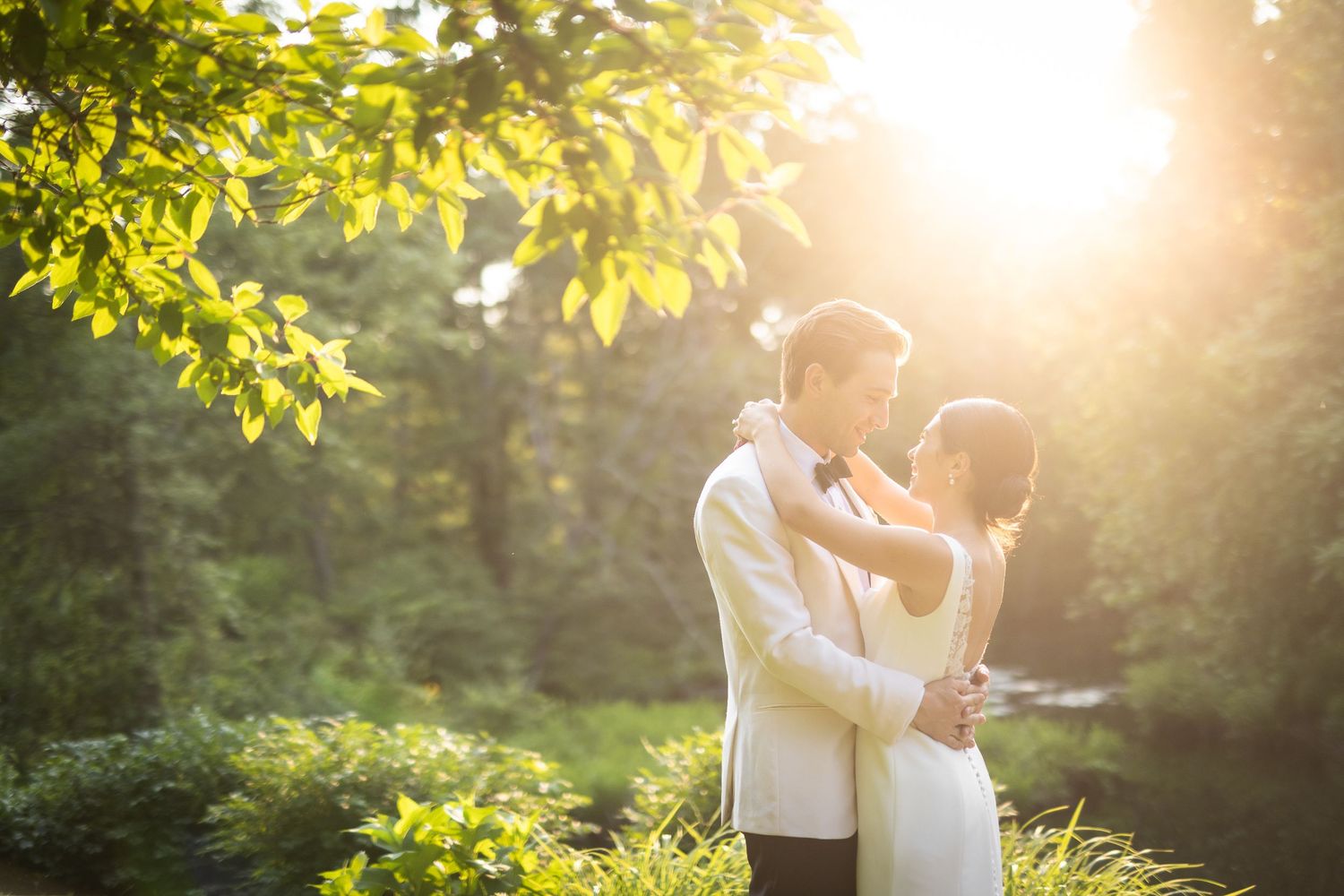 Romantic sunset portrait of couple in white formal attire surrounded by glowing foliage.