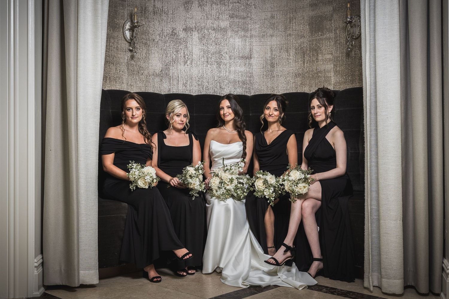 Bridal party in black and white dresses pose against textured wall in formal portraits.