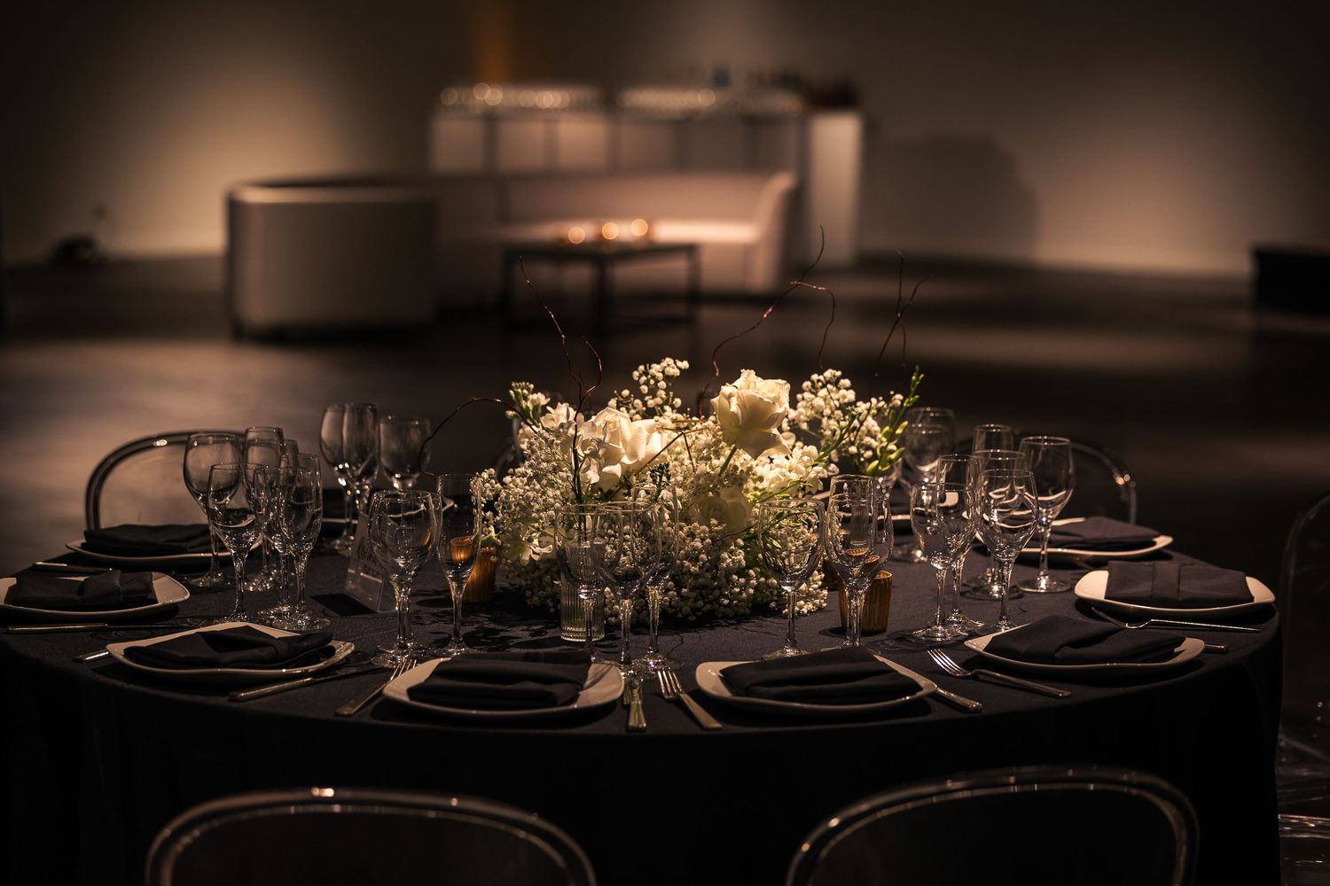 Elegant table settings in dark tones with wine glasses and floral centerpieces create a sophisticated dining atmosphere.