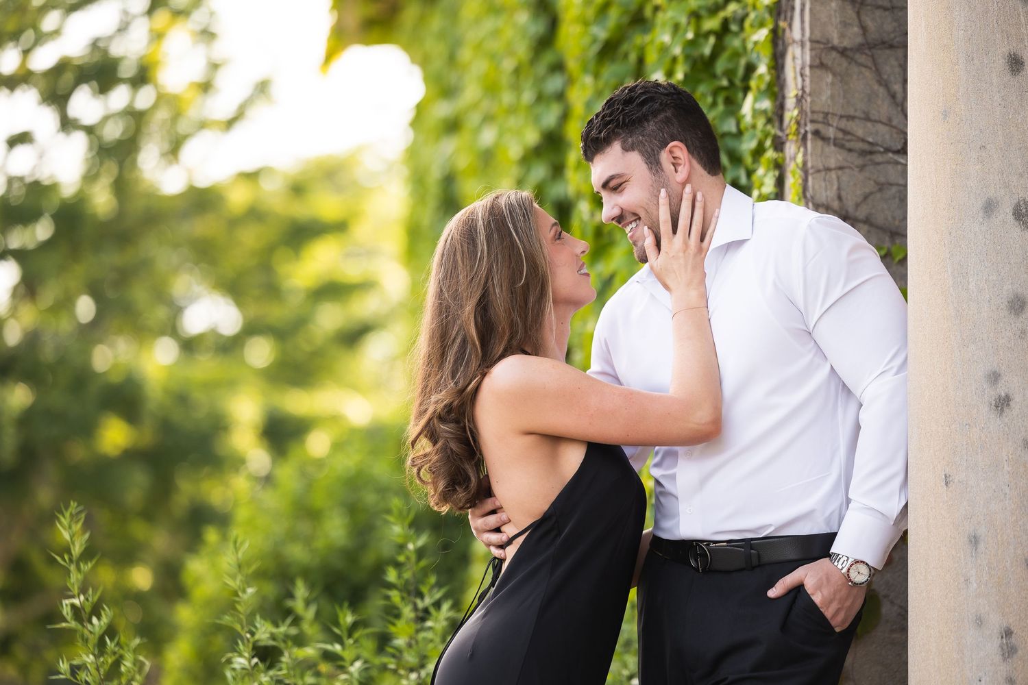 Romantic couple embraces near stone pillars during an outdoor engagement photo session.