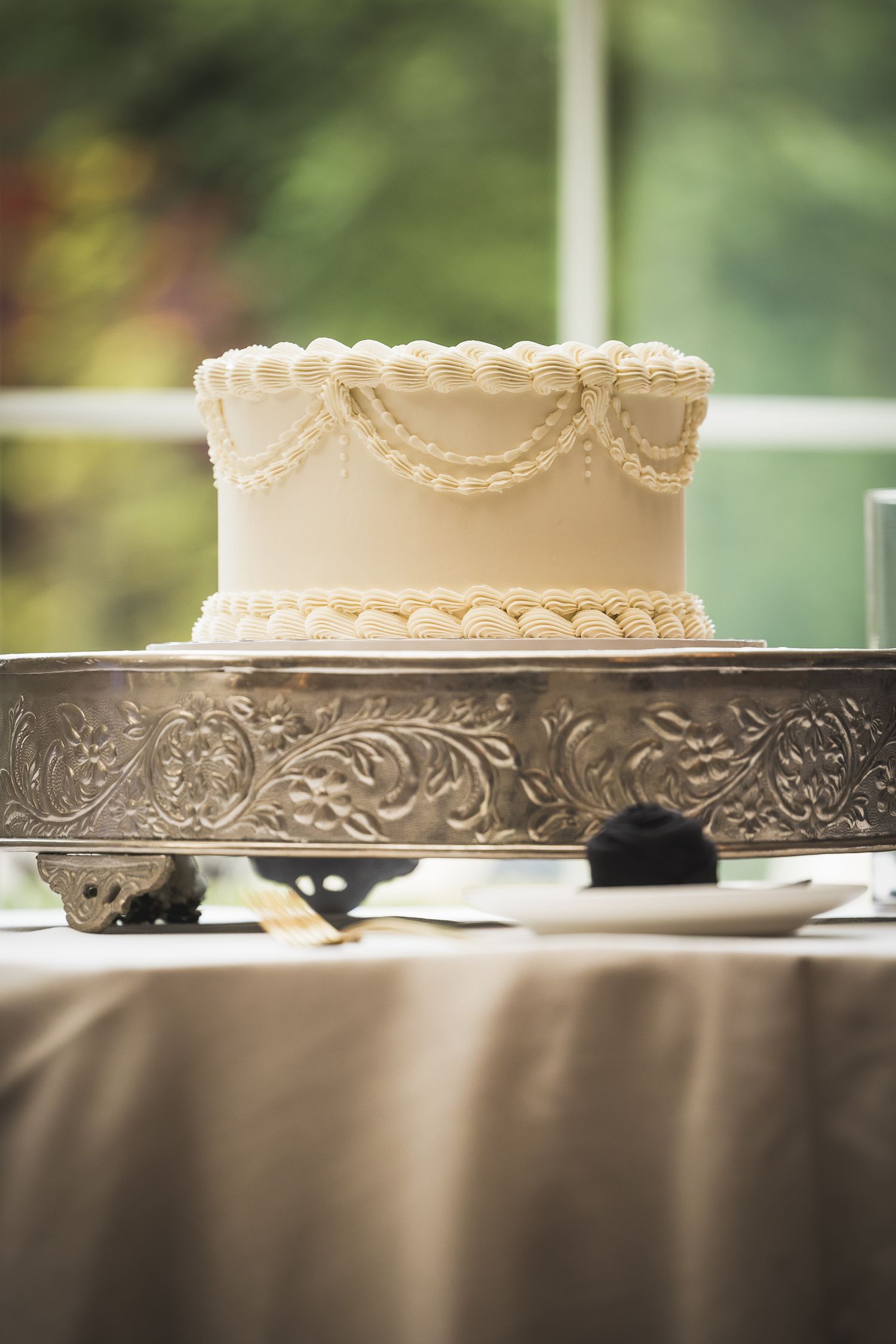Elegant white wedding cake displayed on ornate silver stand with detailed piping.