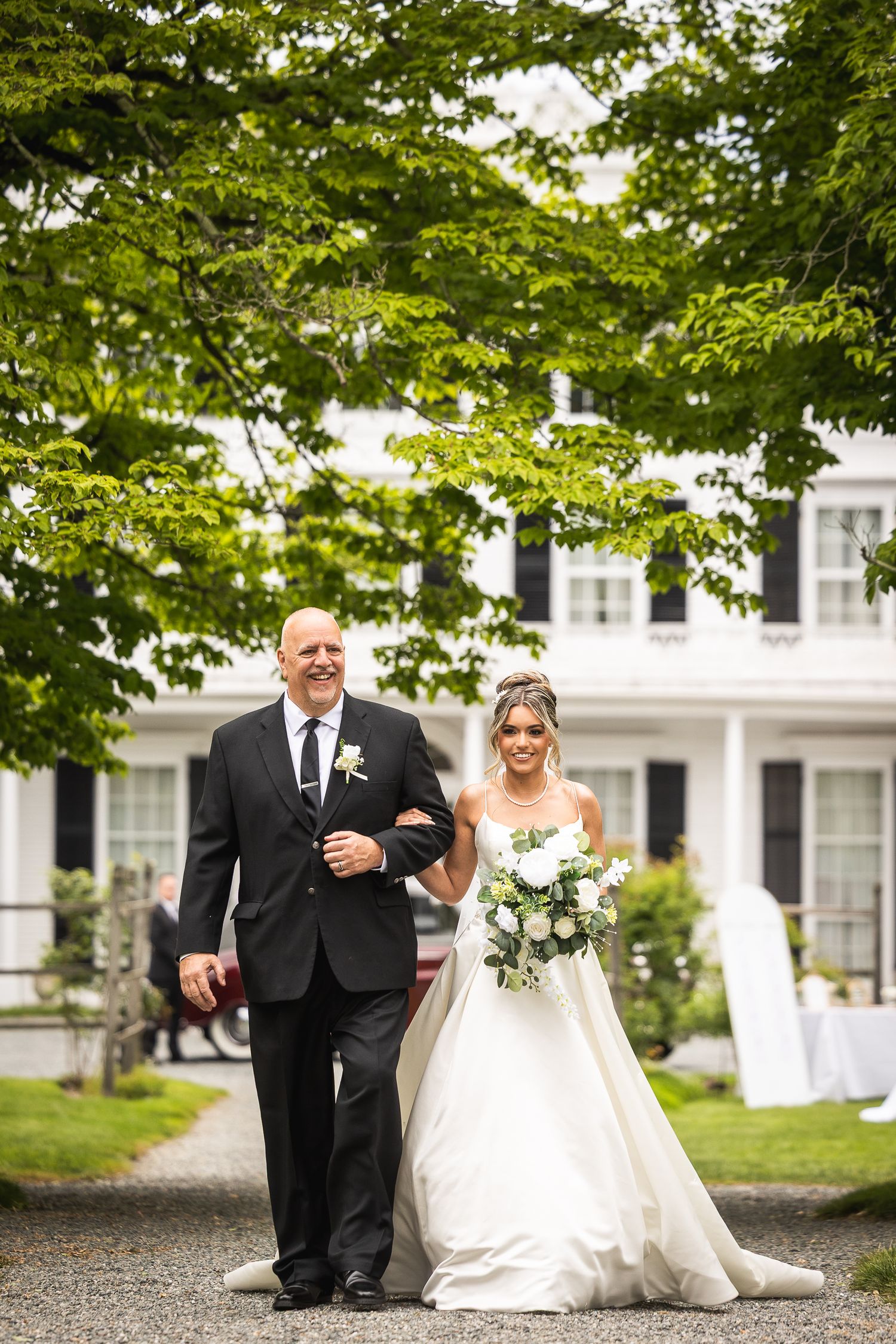 Wedding couple poses playfully on garden path surrounded by lush green trees.