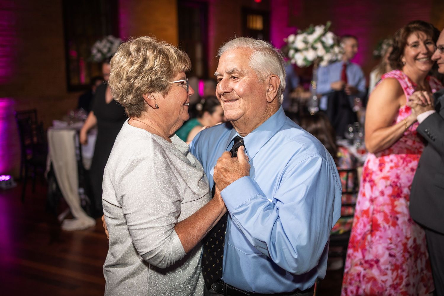 Wedding reception guests dancing and celebrating under purple mood lighting.