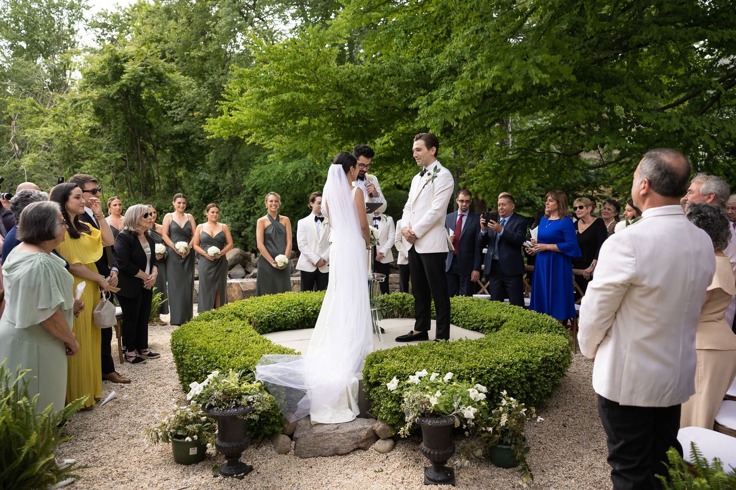 Guests mingle in lush garden setting during wedding celebration.