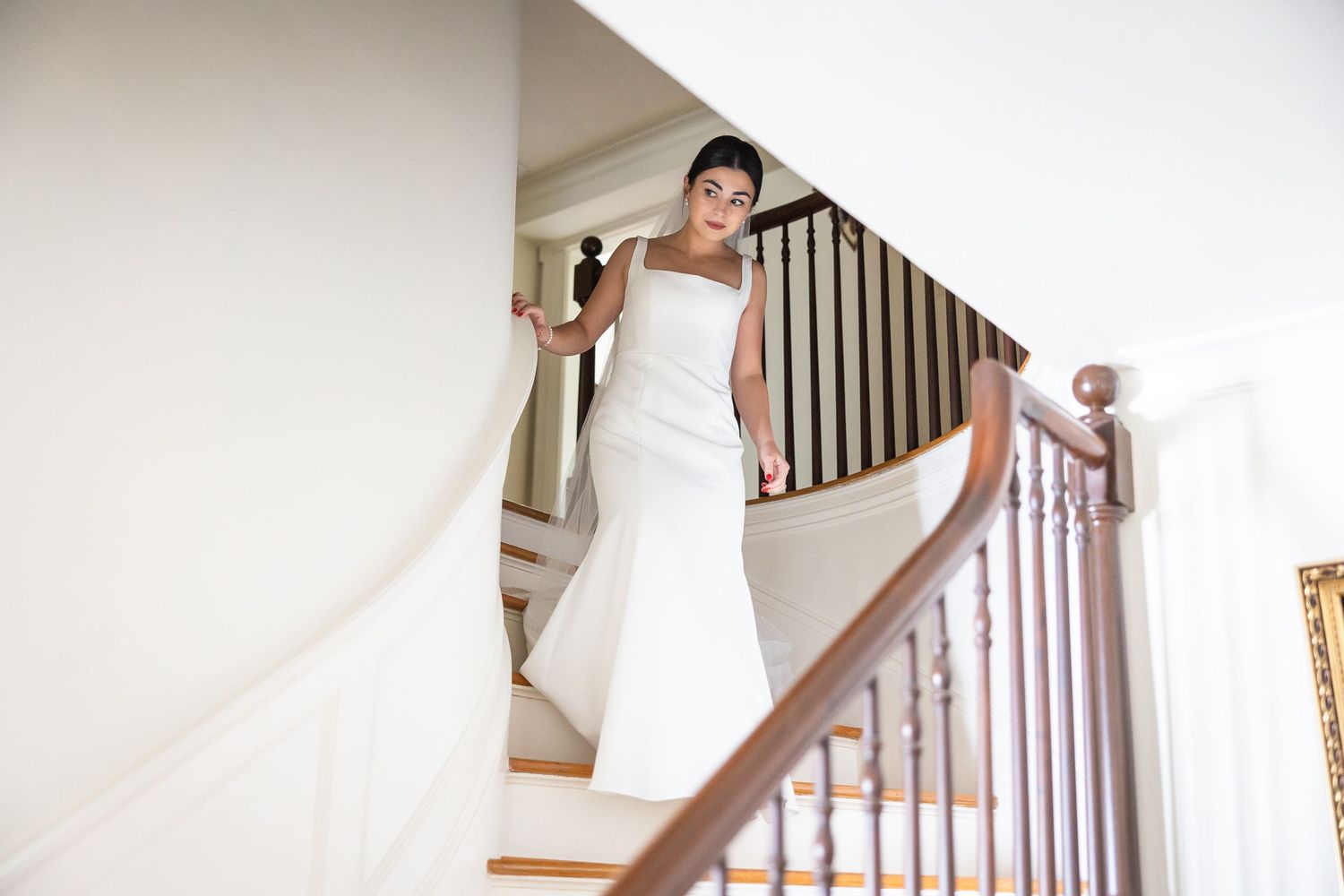 Elegant white wedding dress flowing down wooden staircase in natural light.