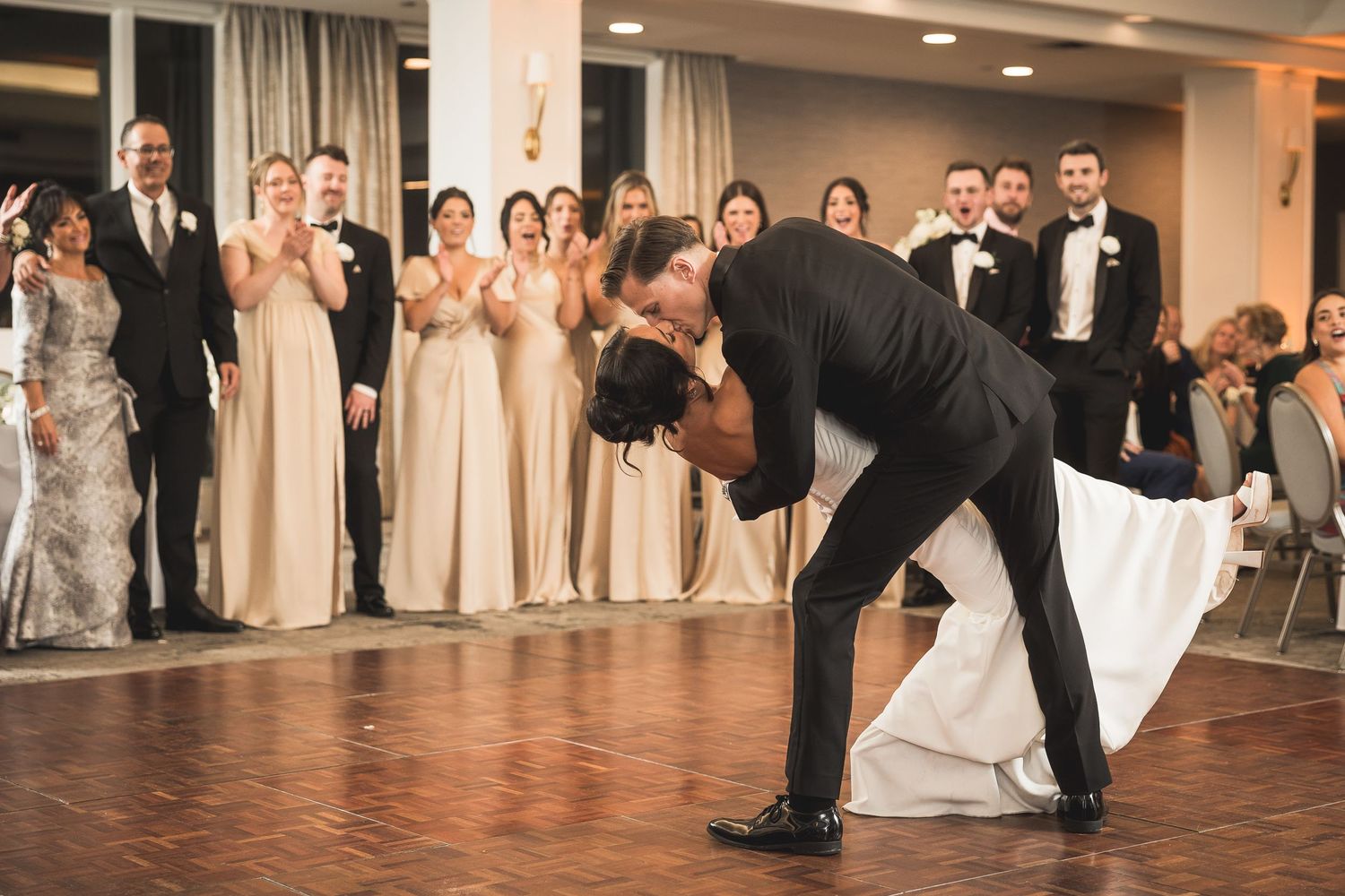 Newlyweds share their first dance surrounded by wedding party members in formal attire.