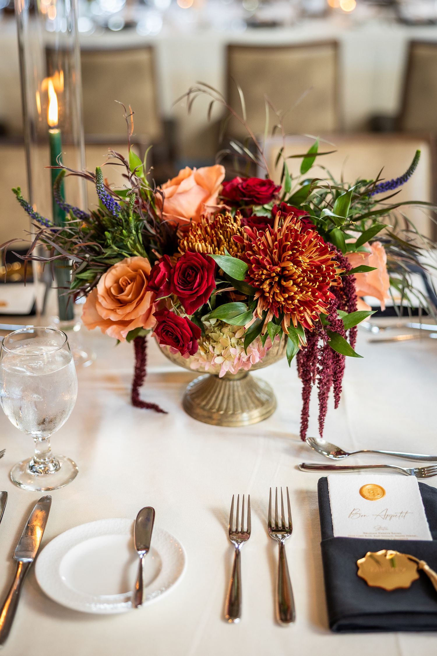 Elegant table setting with autumn floral centerpiece featuring peach roses, red dahlias, and burgundy amaranth blooms.