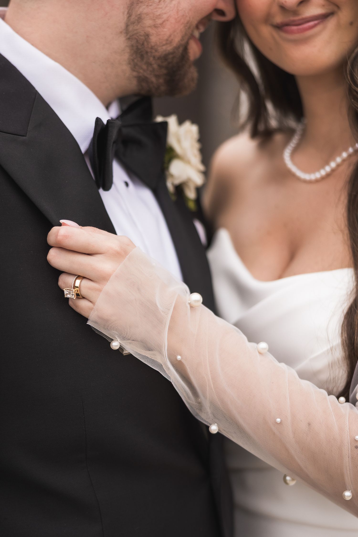 Elegant wedding attire details with pearl necklace, sheer gloves, and formal black tuxedo.