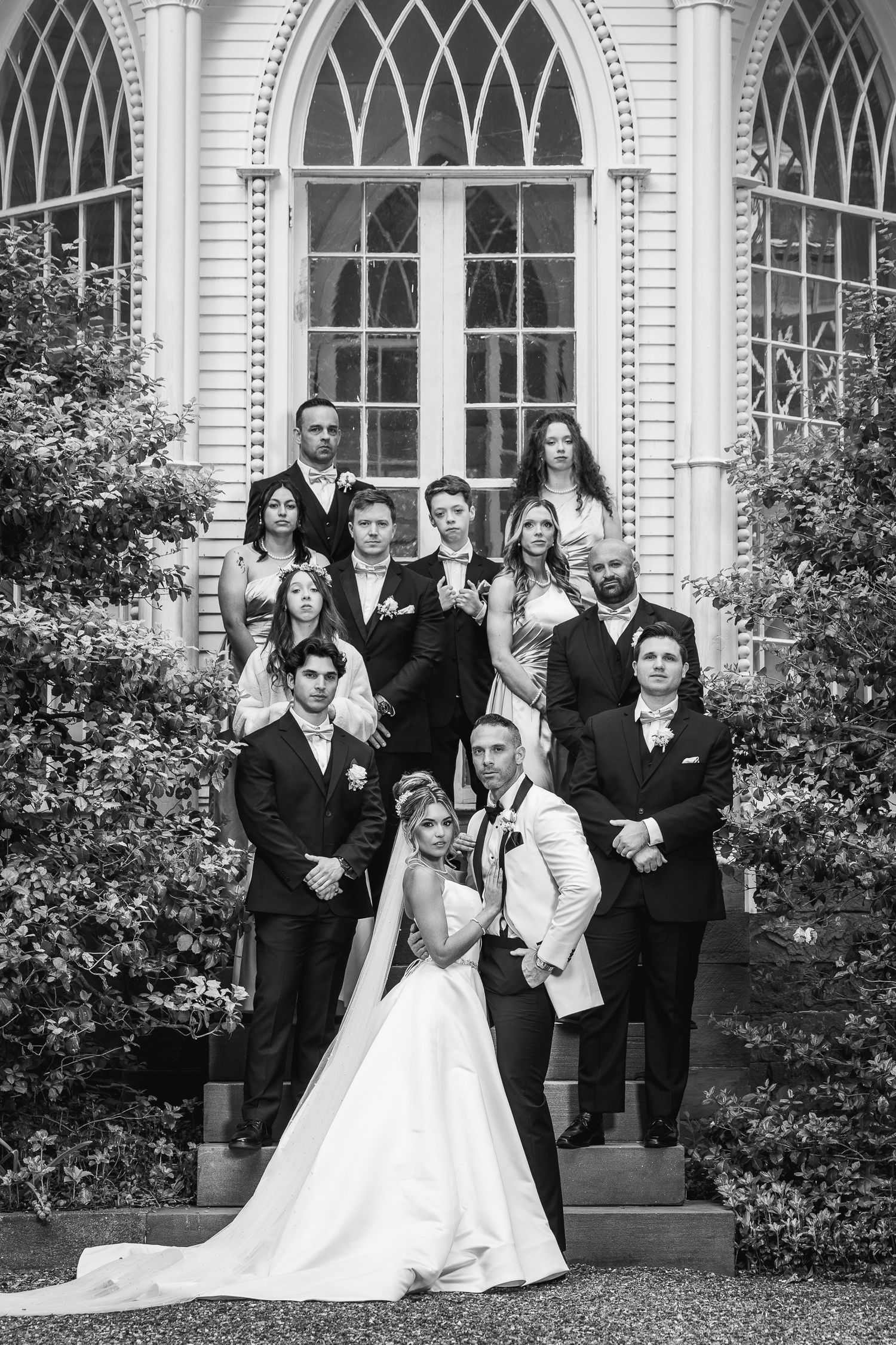 Wedding party poses in front of a classic white building with arched windows.