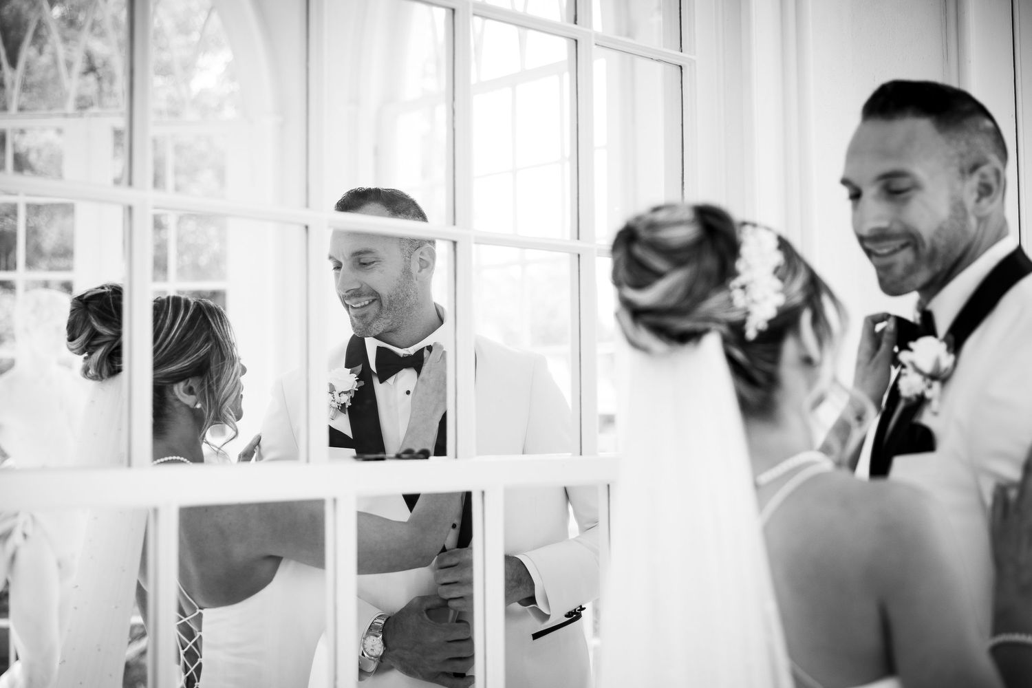 Black and white candid moments of wedding party getting ready in bright window-lit room.